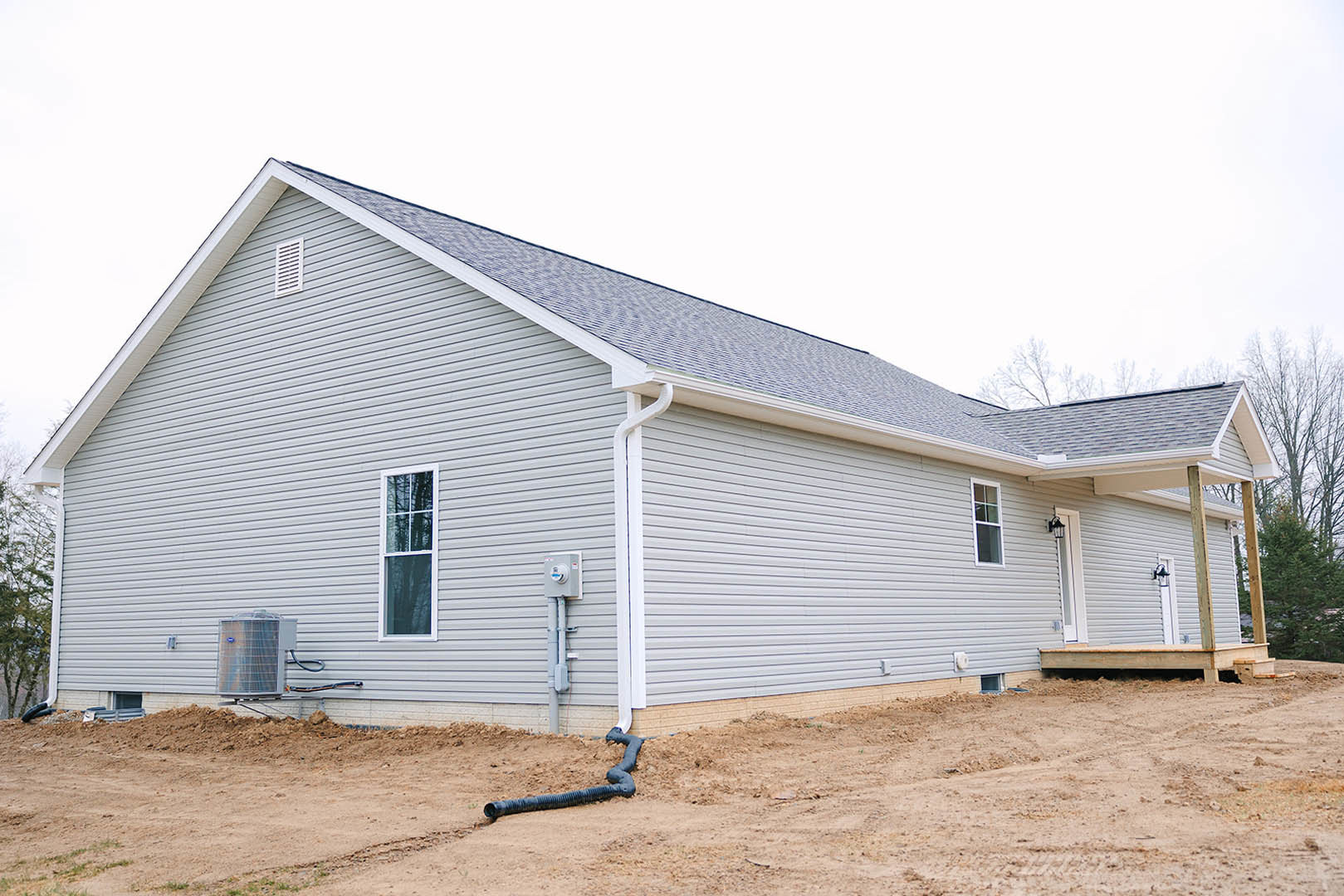 Modern house with white roof, light-colored siding, large grassy yard, mature trees, visible air conditioning unit, white-framed windows, and outdoor shed.