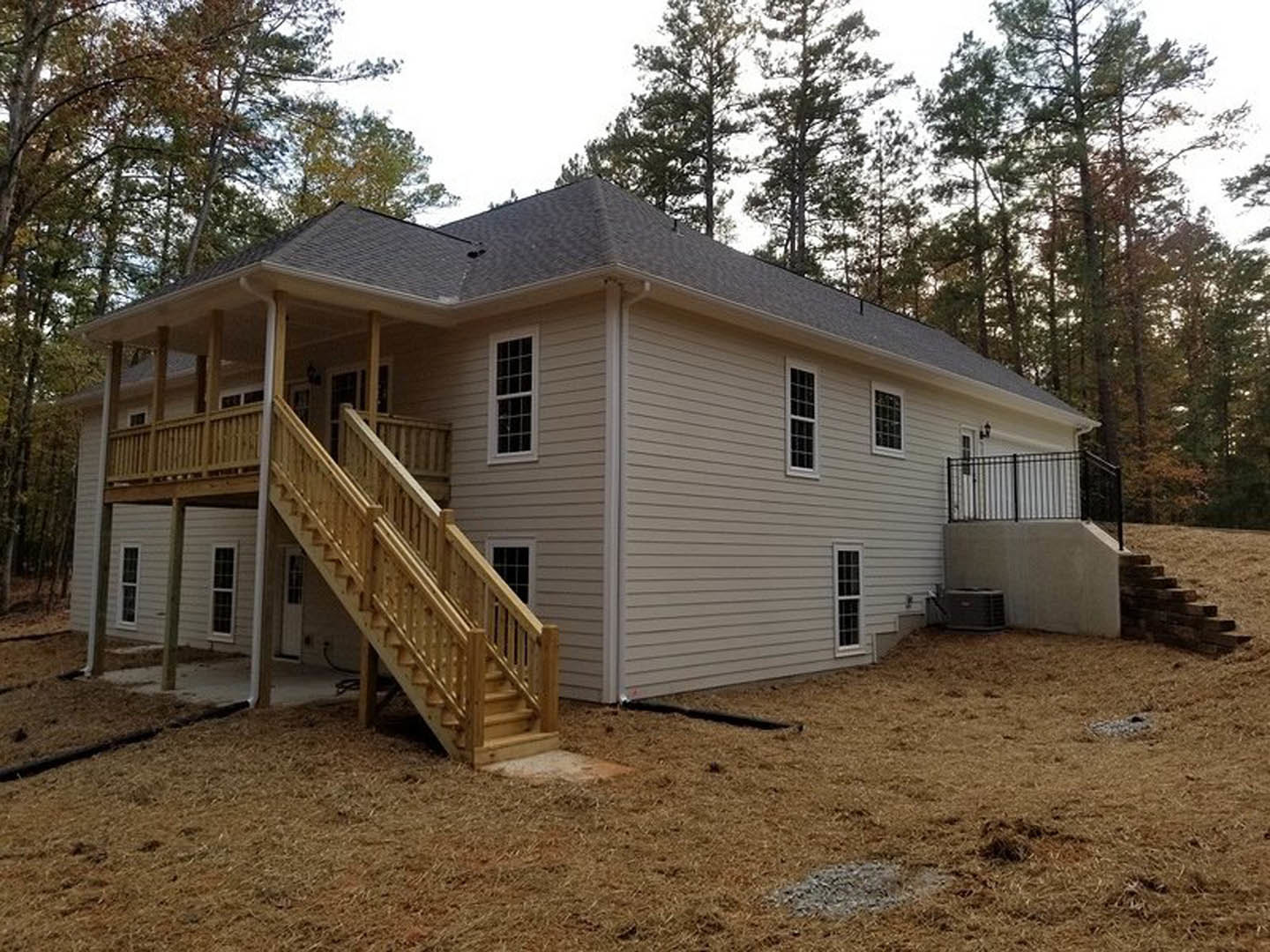 Wooden exterior staircase leading to porch, white-framed window, black metal fence atop white wall, landscaping with rocks, tree in background
