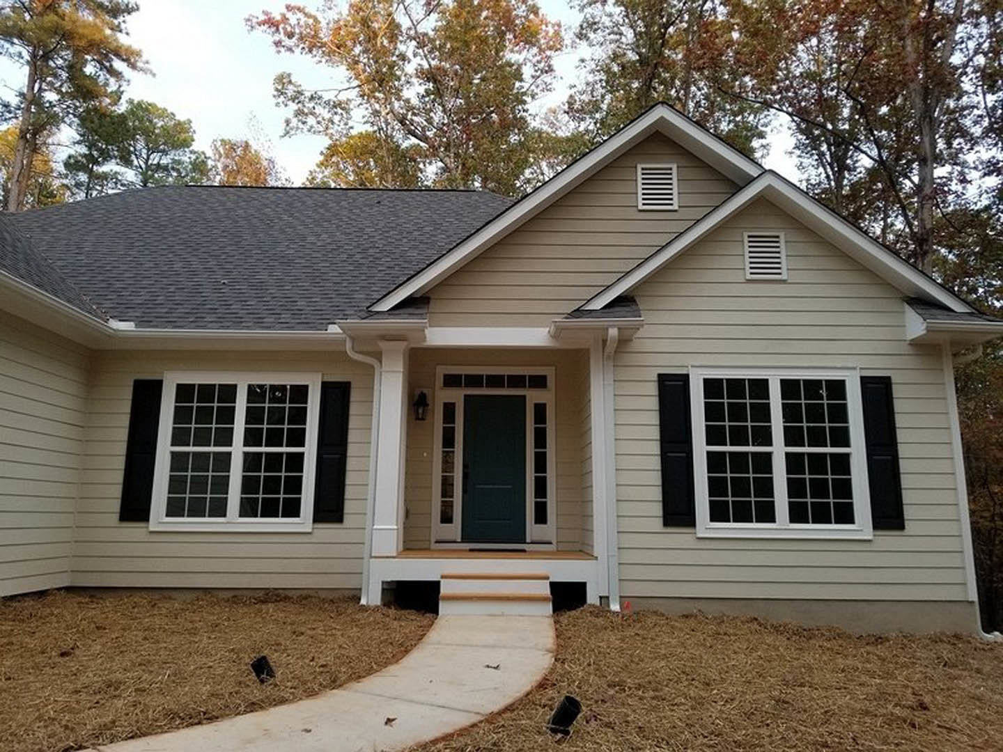 White cottage with horizontal siding, gabled roof, and front porch; stone walkway leads through landscaped yard with mature trees.