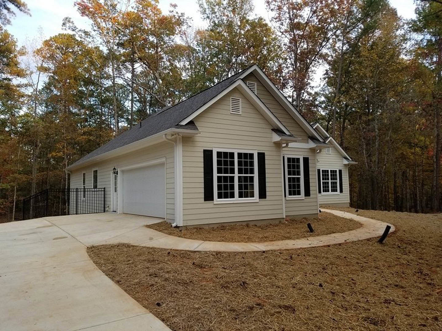 Two-story house with white siding, black shuttered windows, attached garage, concrete driveway, grassy yard, mature trees, and white fence along the side.