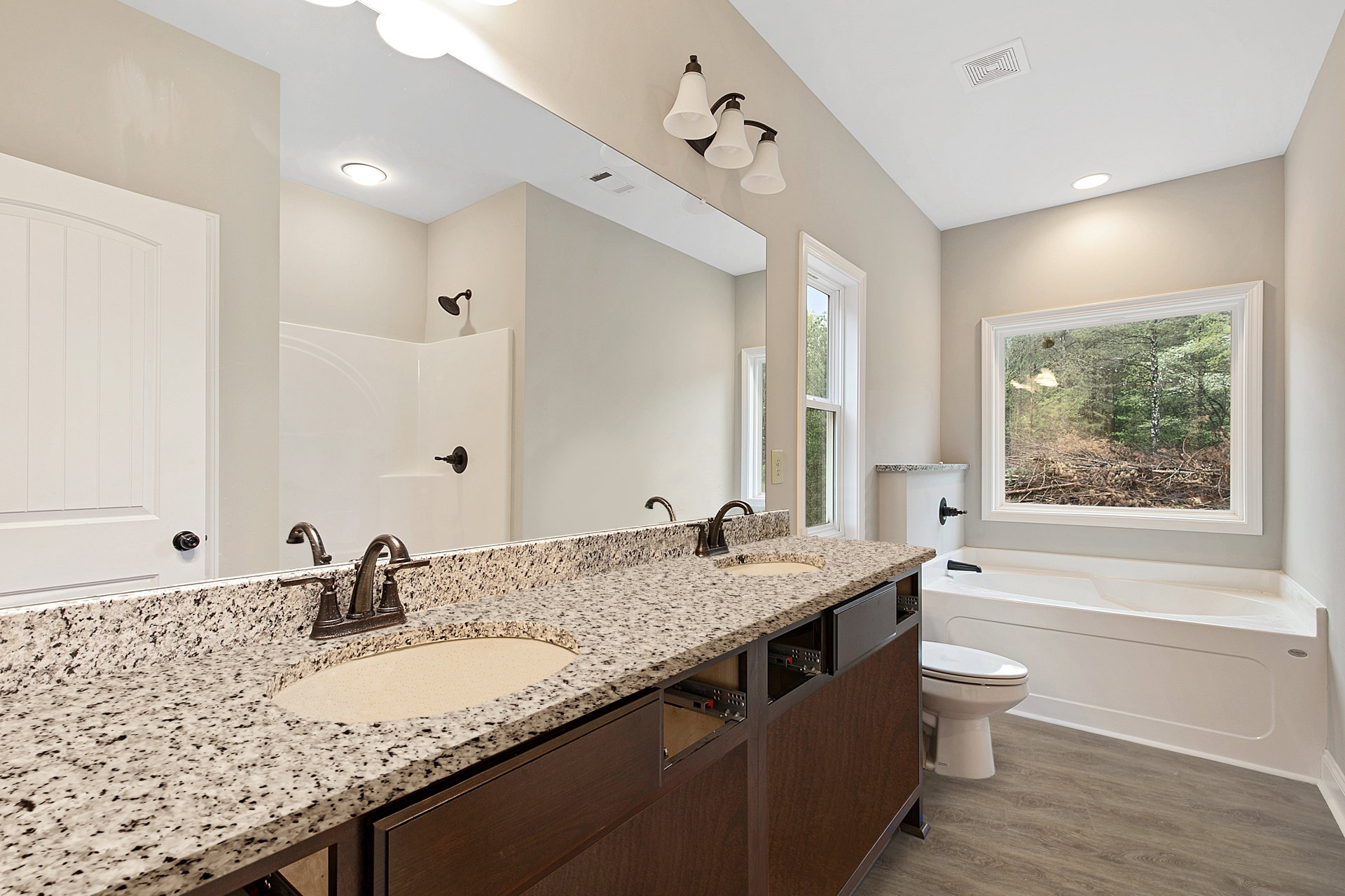 Bathroom featuring marble countertops, undermount sink with chrome faucet, white toilet, three-light fixture above mirror, large window overlooking forest, light tile flooring, and