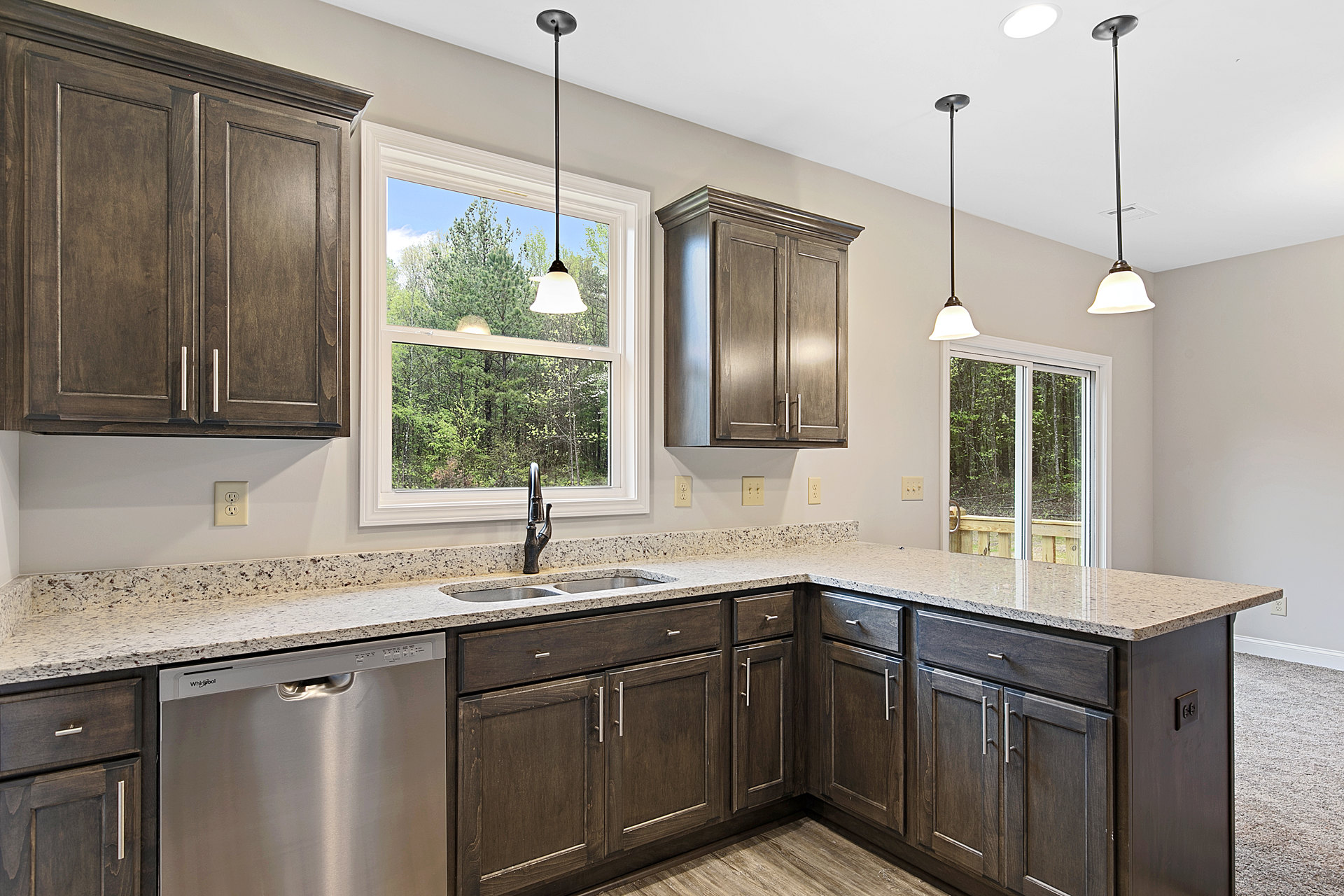 Modern kitchen featuring white tile backsplash, stainless steel sink with chrome tap, wooden cabinets with metal handles, built-in dishwasher, stone countertop, bell-shaped pendant
