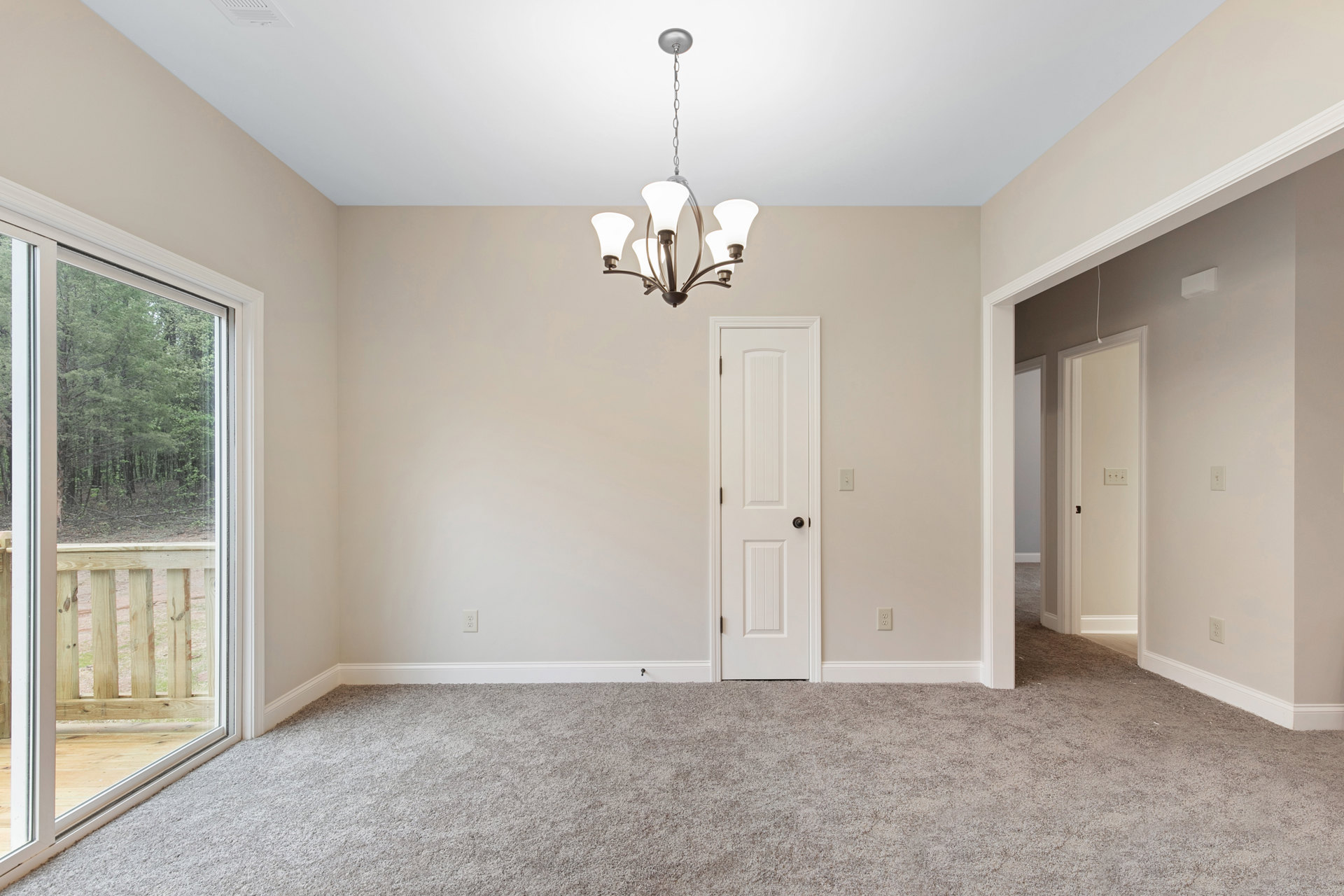 Chandelier with glass accents hanging from white ceiling, white paneled doors with black hardware, laminate wood flooring, large window framing forest view, white plaster walls