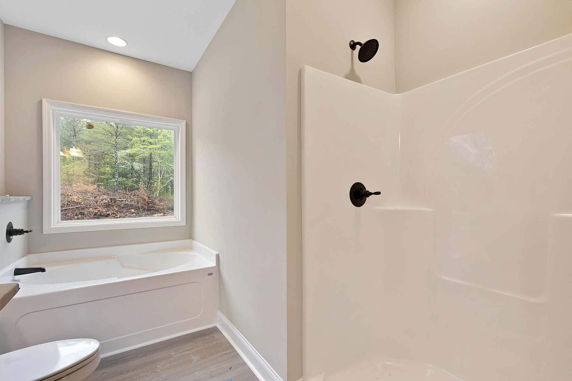 White tile bathroom featuring a glass-enclosed shower with round shower head, freestanding tub beside a window overlooking forest, modern sink and tap, close-up of wall switch and