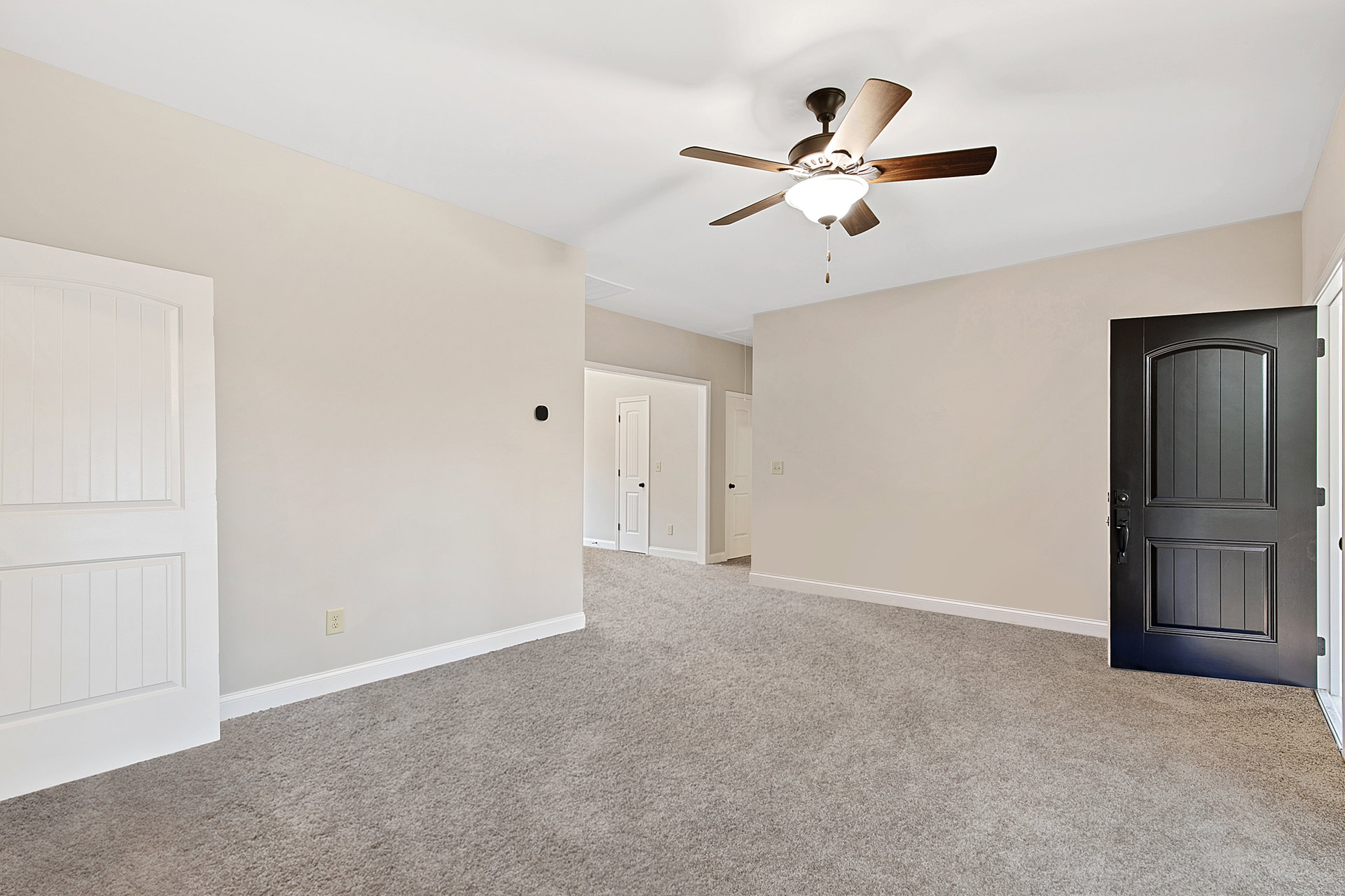 Carpeted room with white walls, black paneled door, ceiling fan with integrated light fixture