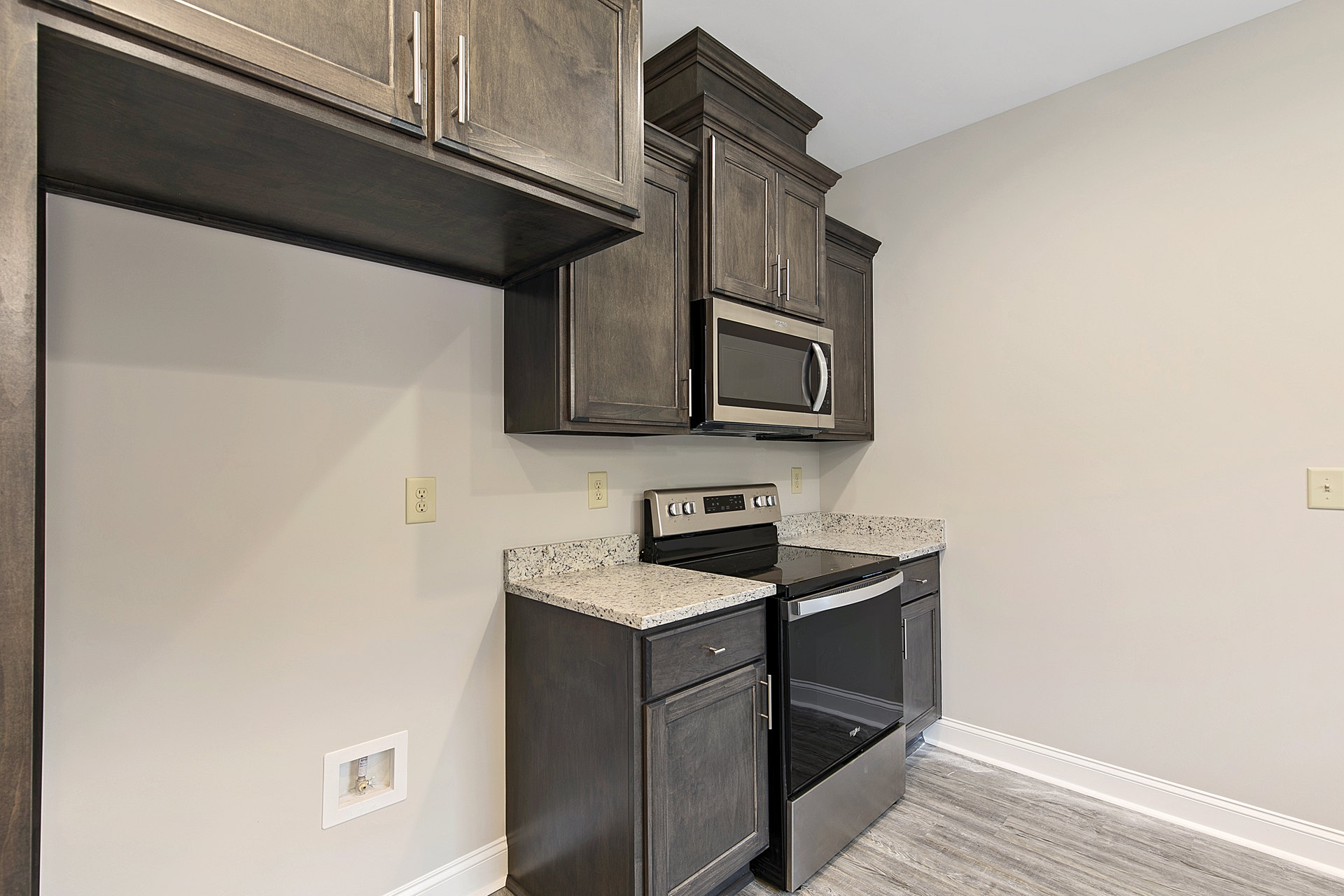 Modern kitchen featuring white cabinetry, stainless steel appliances including an open microwave, black dishwasher, white countertop, black floating shelf, and a glass door.