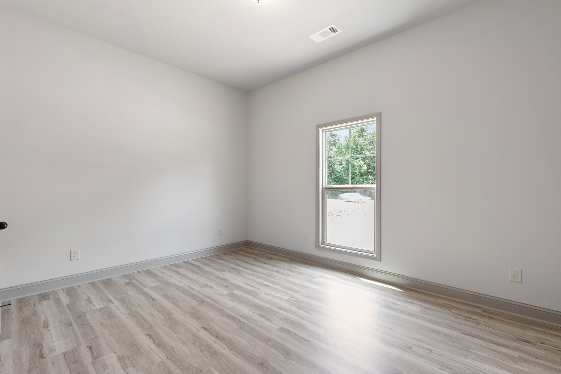 Hardwood floor room with large window overlooking trees and parked car, white ceiling vent, plaster walls
