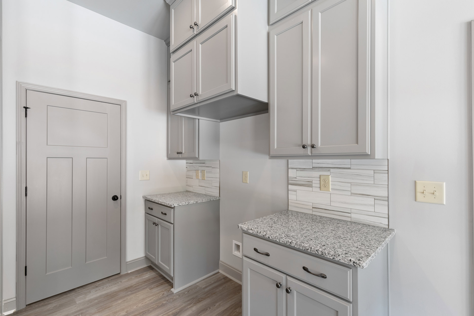 White kitchen with marble countertops, shaker cabinets, black hardware, double light switch on wall, and white door with black knob.