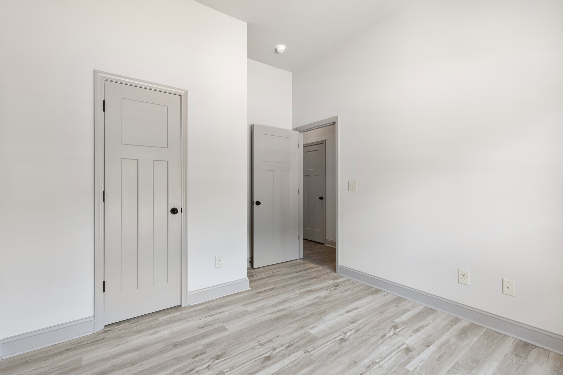 White walls and ceiling, wood laminate flooring, white door with black knob, minimalist interior design