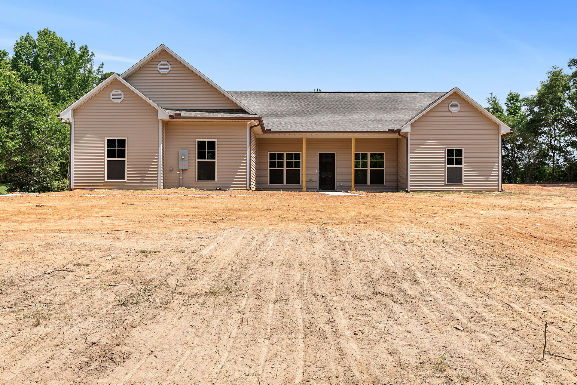 White-framed window and black door on light-colored farmhouse, surrounded by dirt field and sparse trees under blue sky