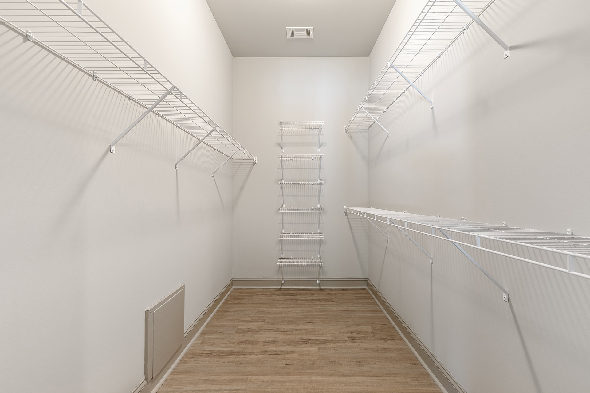 White built-in shelves against smooth plaster walls, light wood flooring, ceiling vent, and a white storage box placed on the floor.