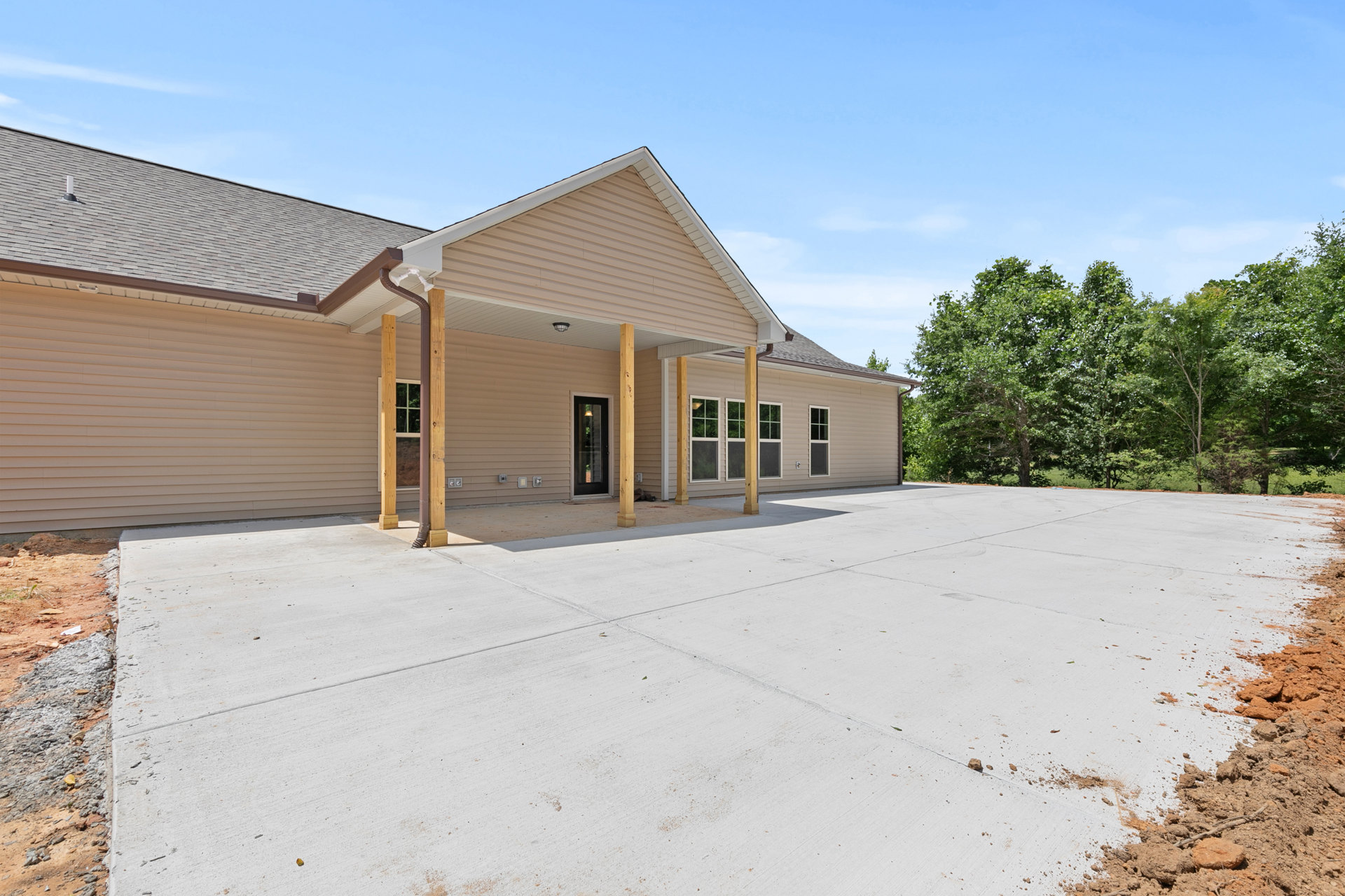 Modern two-story home with black-framed glass door, large windows, covered porch, paved driveway, and mature trees surrounding the front yard