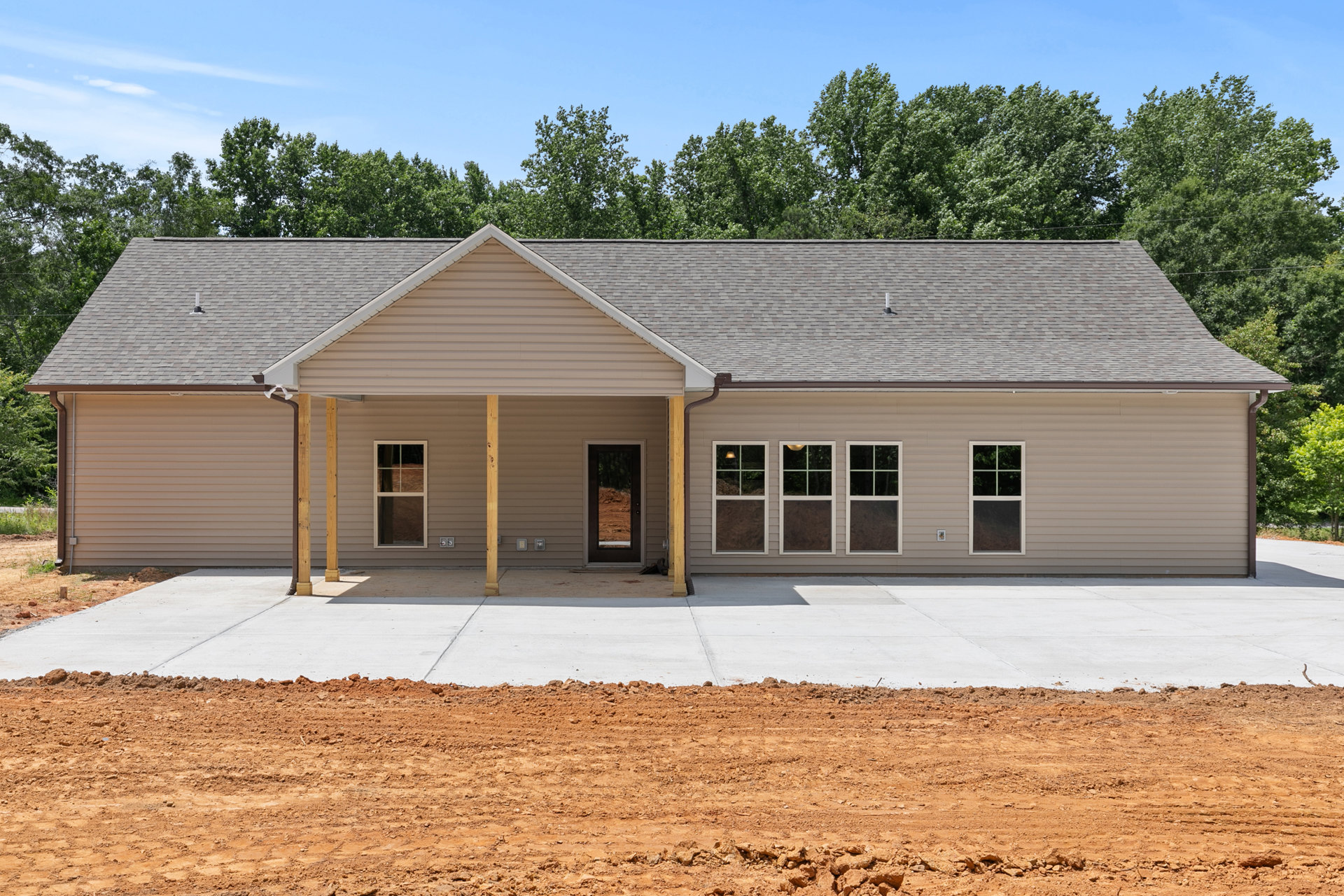Two-story house with white siding, covered front porch, white-framed windows, paved driveway leading to a dirt road, surrounded by trees and open ground.