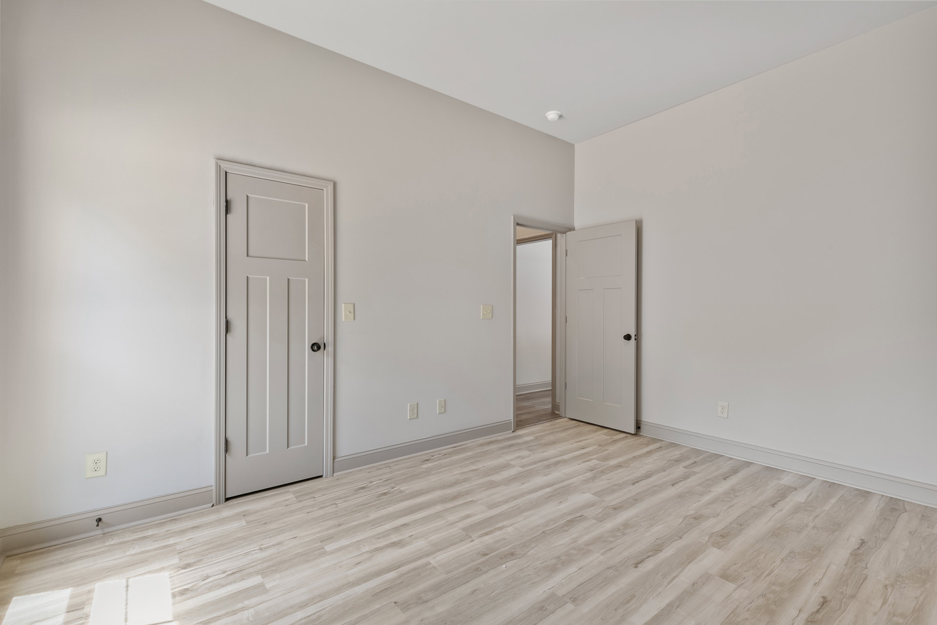 Wood flooring in a room with two white doors, white walls, black door knobs, and light switches.