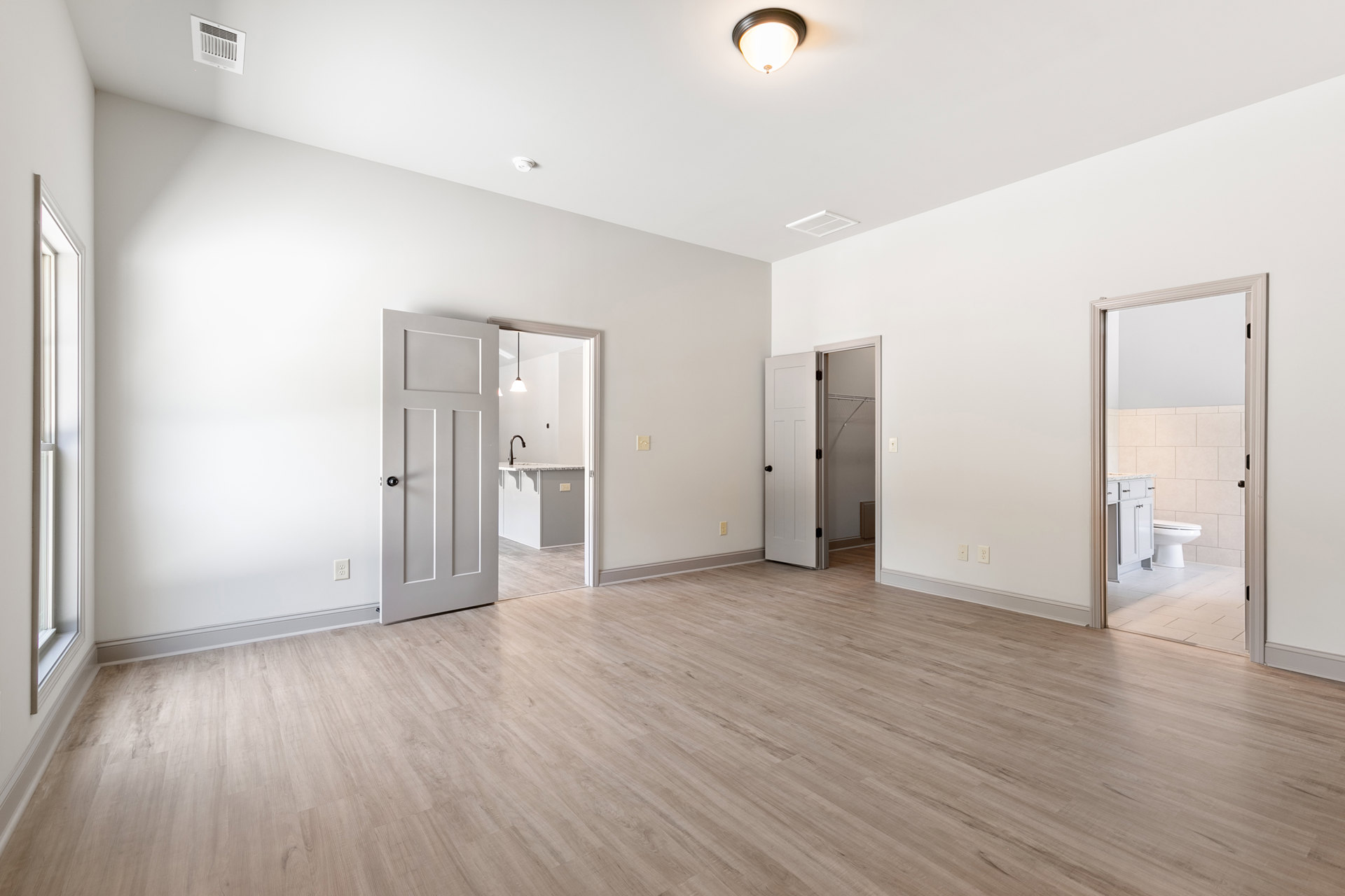 White walls and wood flooring in a residential room with an open door, white vent, and modern light fixture visible.