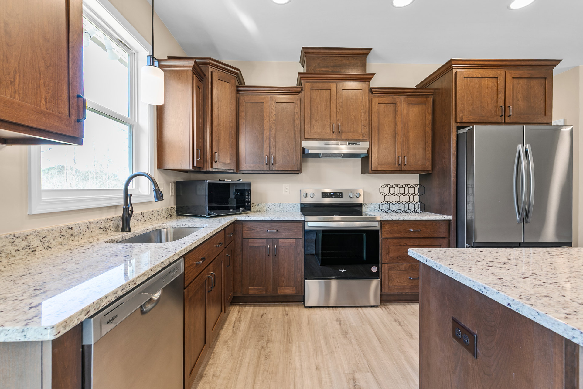Granite countertops, wood cabinets, stainless steel oven and refrigerator, black appliance with red indicator light, white device with illuminated button, kitchen sink against