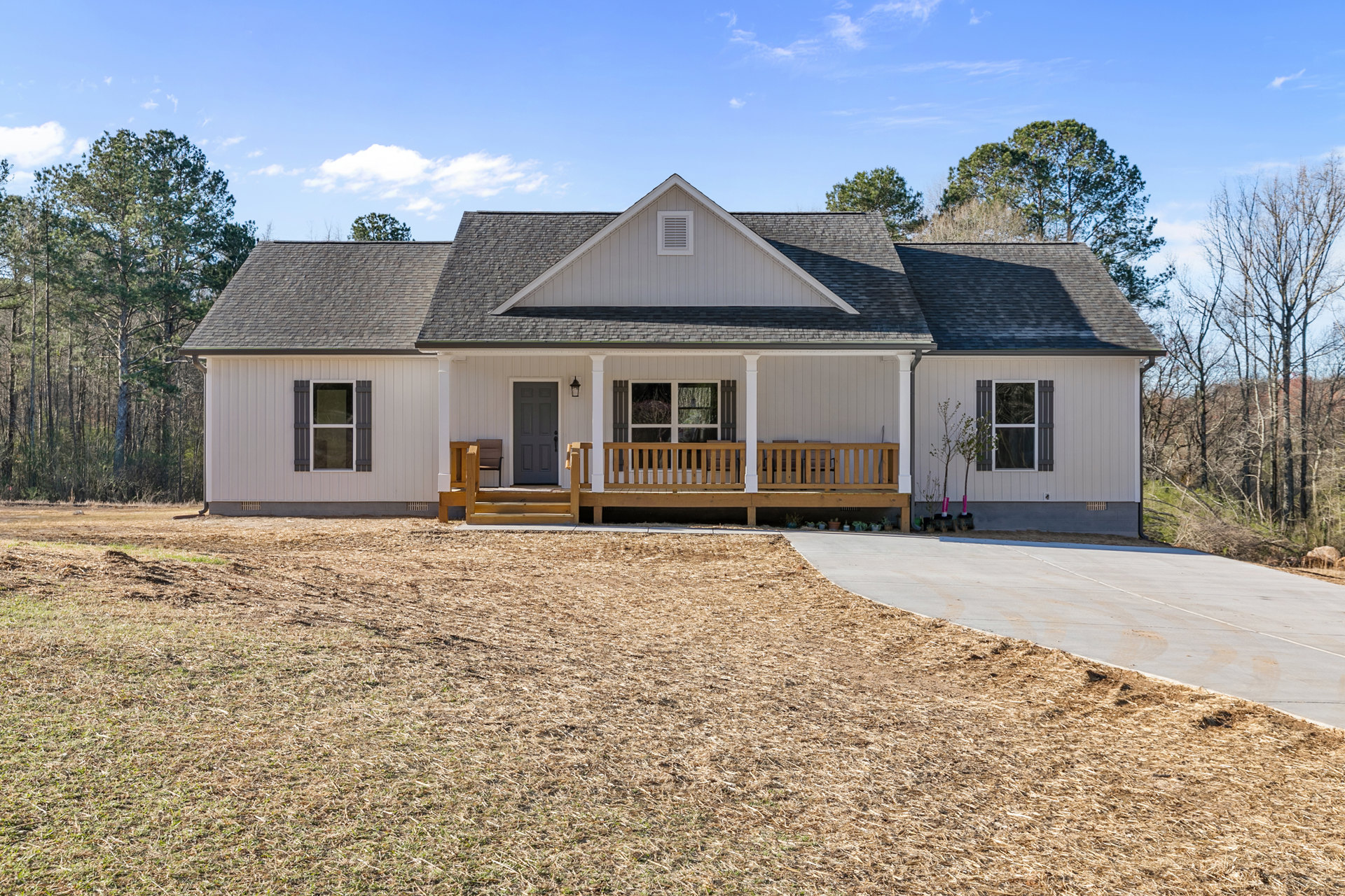 Two-story house with grey siding, white trim, covered front porch with wooden bench, concrete driveway, green lawn, large windows, and grey front door