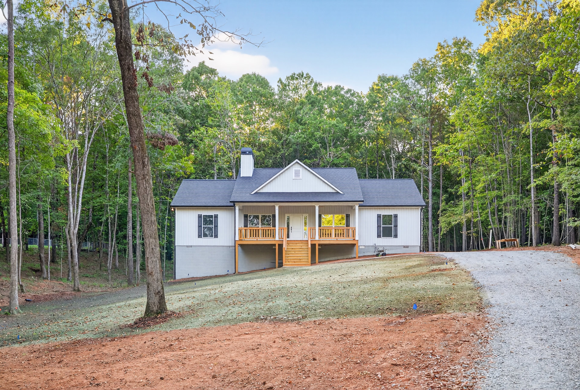 Wood-clad house with covered front porch, paved driveway, large windows, surrounded by tall leafless trees and natural woodland landscaping
