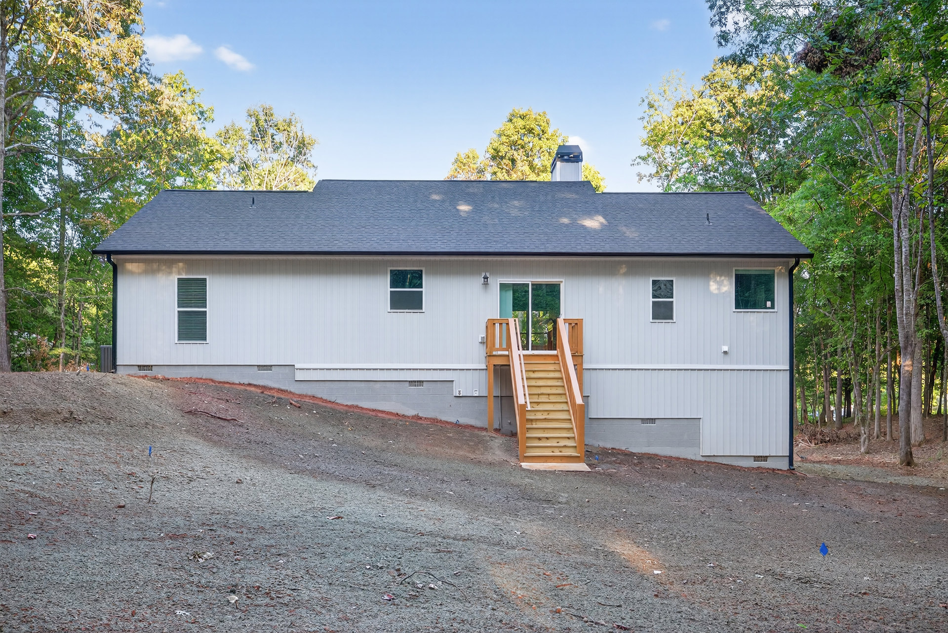 Two-story home with exterior wooden staircase, white siding, large windows, and surrounding trees under a partly cloudy sky