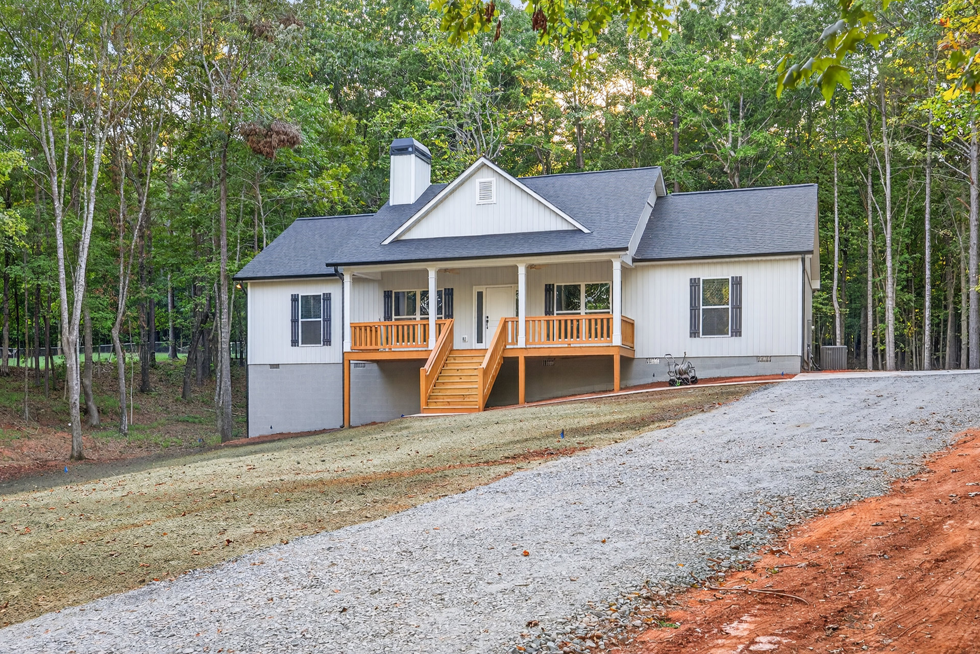 Two-story home with white-framed windows, wooden porch and staircase, concrete driveway, and mature trees in landscaped front yard