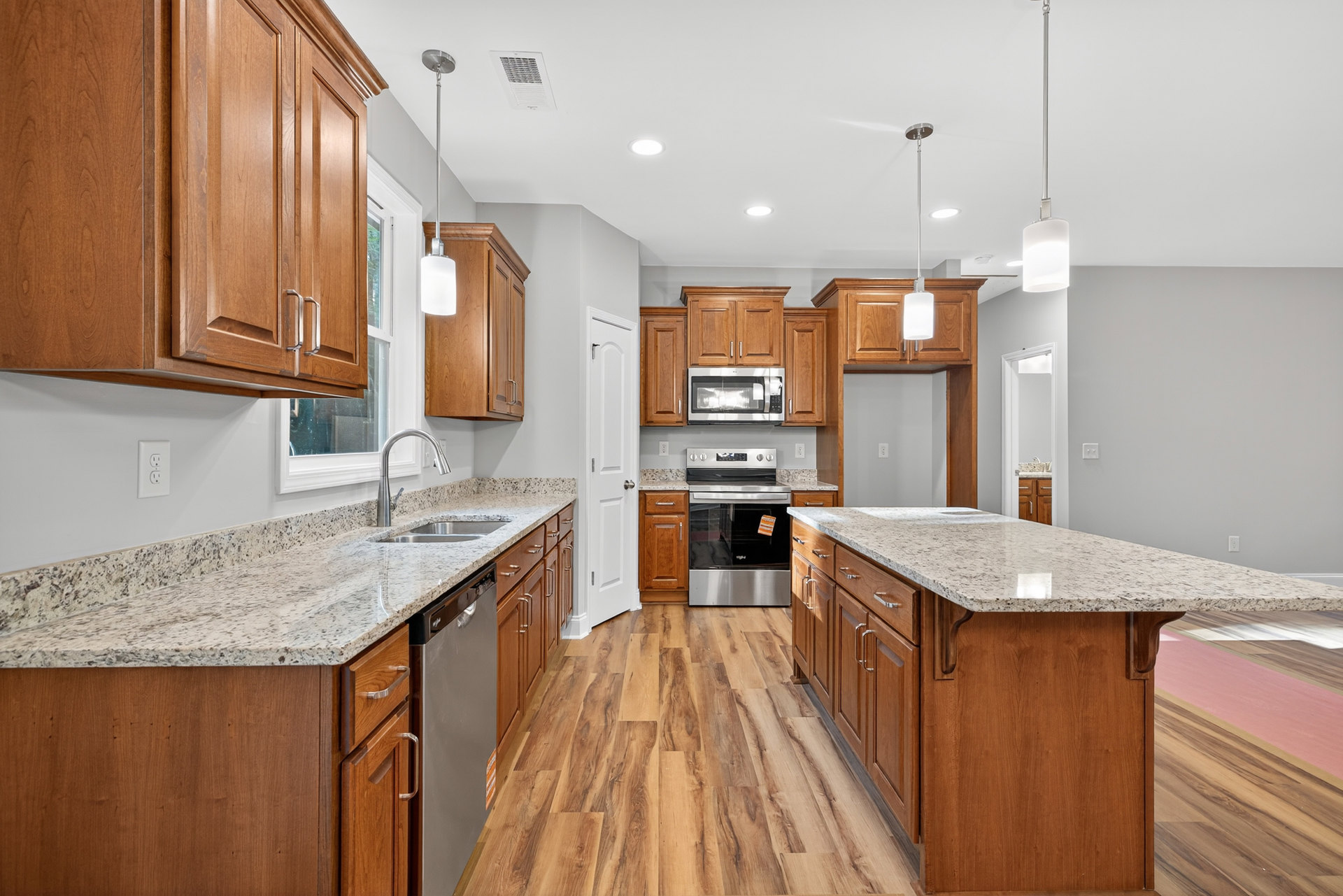 Granite kitchen island with stainless steel appliances, white cabinetry, built-in oven and microwave, silver hardware, and undermount sink