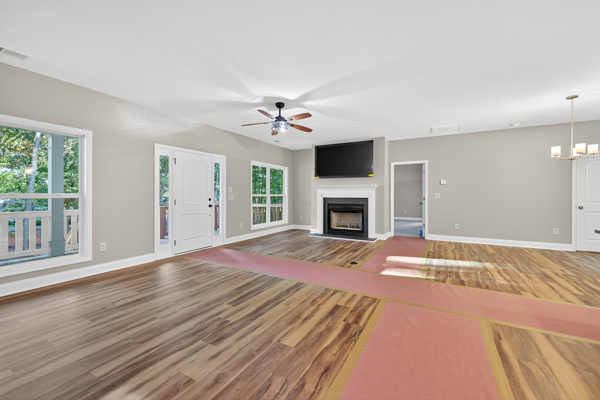 Living room with wood flooring, white walls, glass-front fireplace, ceiling fan with light, black TV on white console, white door with matching frame