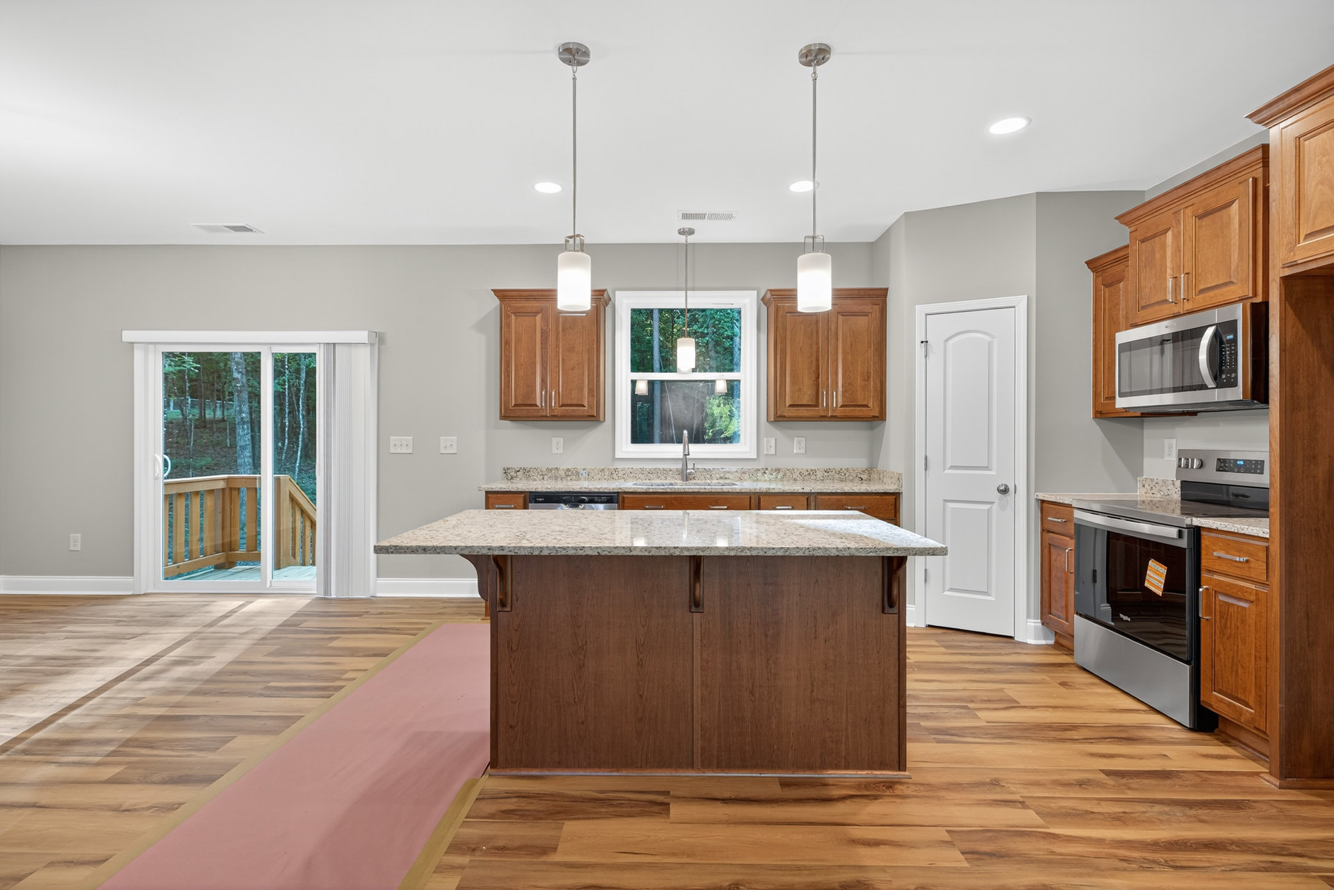 Spacious kitchen featuring a large granite island, white cabinetry, stainless steel stove, built-in microwave, and sliding glass door overlooking a forest.