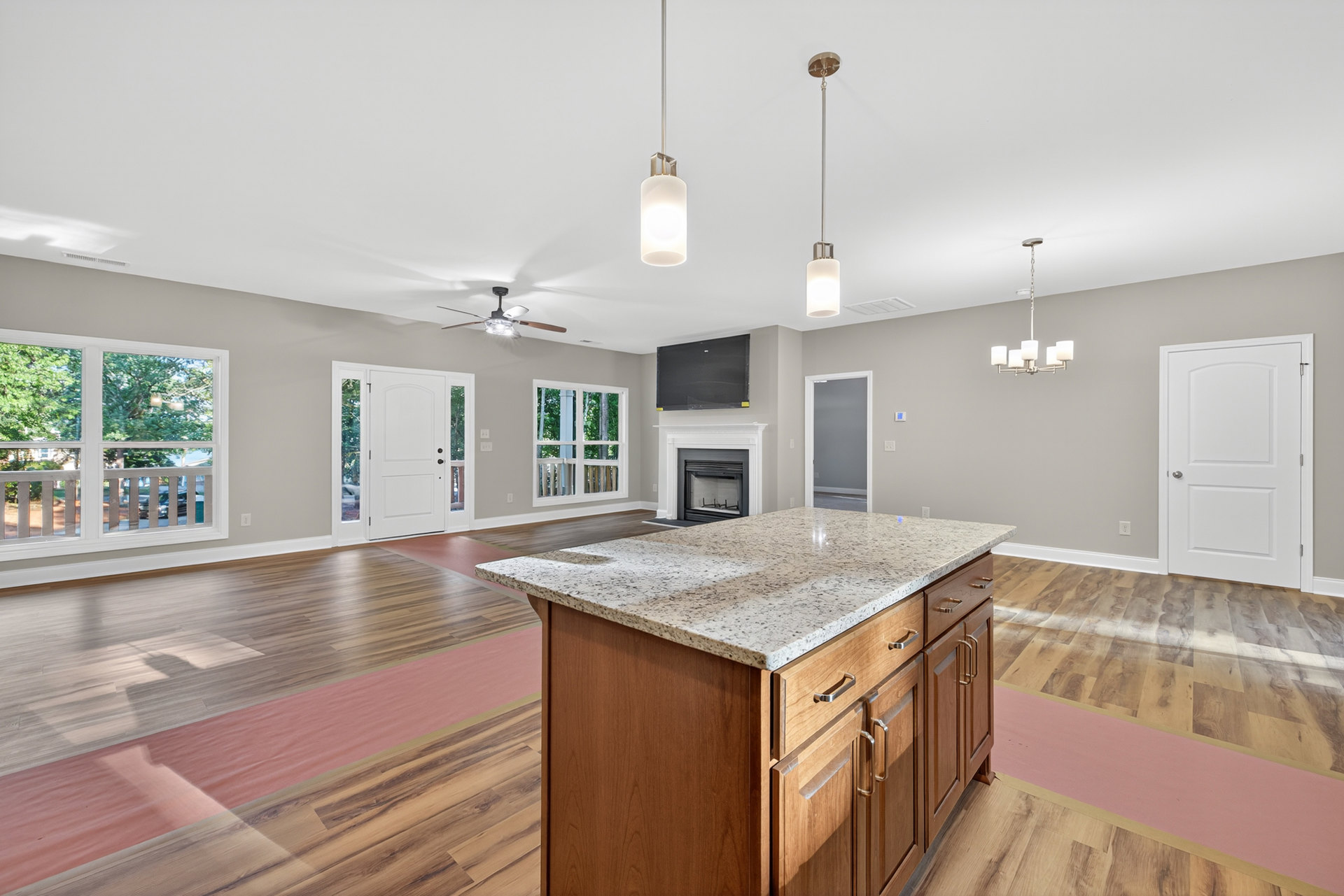 Kitchen island with granite countertops, white cabinetry, stainless steel sink, and pendant lighting in a spacious room; fireplace with stone surround, white door with silver