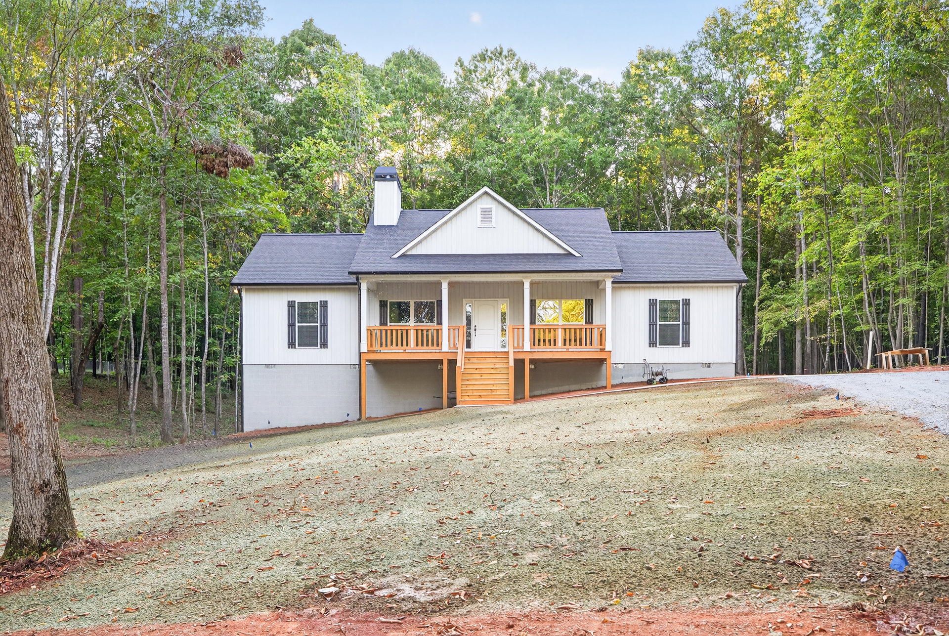 Two-story home with white-framed windows, covered front porch, wooden staircase, expansive green lawn, and mature trees in the yard