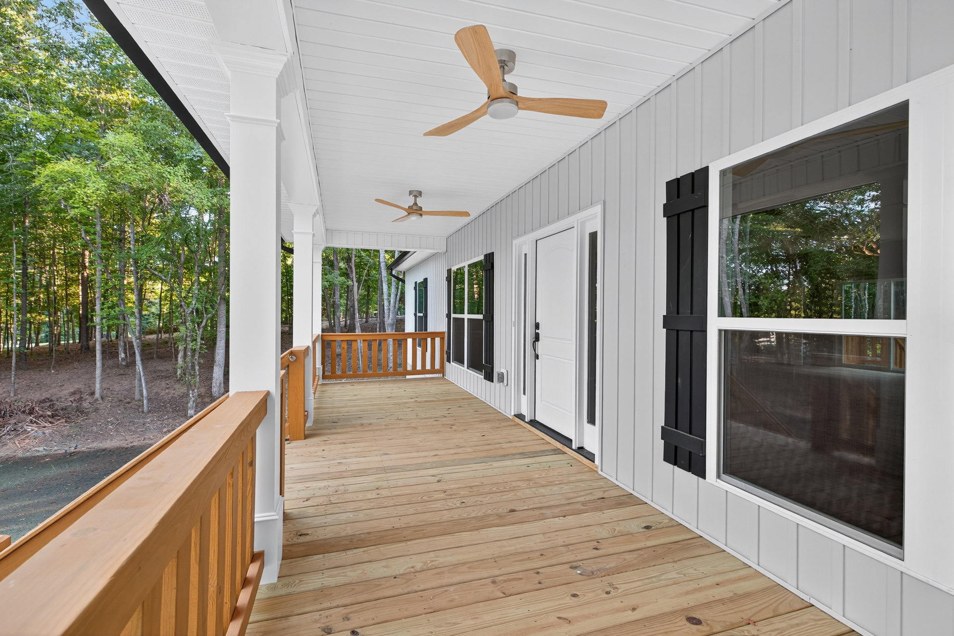Covered porch with wood deck, ceiling fan with light fixture, wooden railing, bench, and windows overlooking trees
