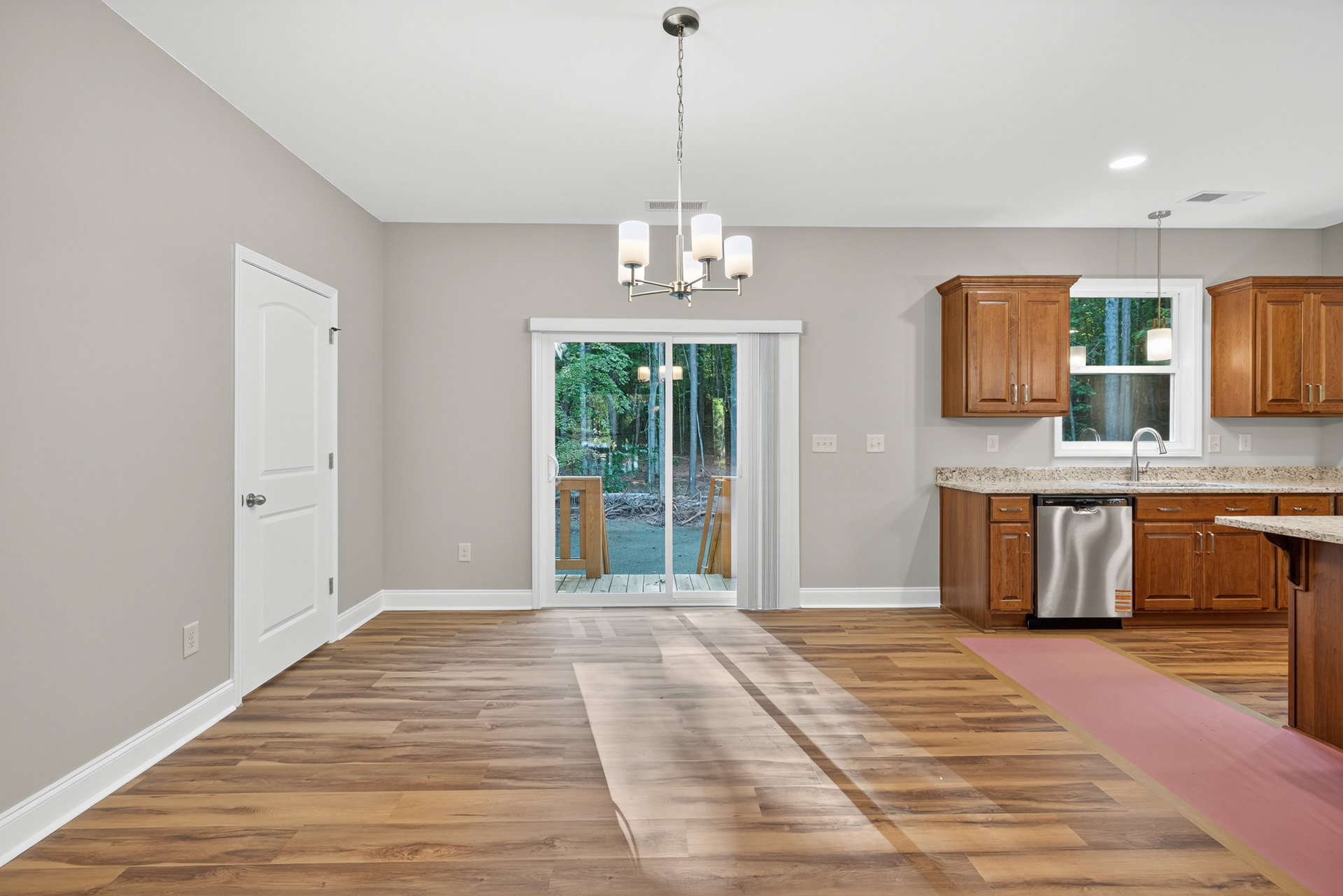 Open kitchen and dining area featuring wooden cabinets, silver dishwasher, hardwood flooring, and a sliding glass door overlooking a forest.