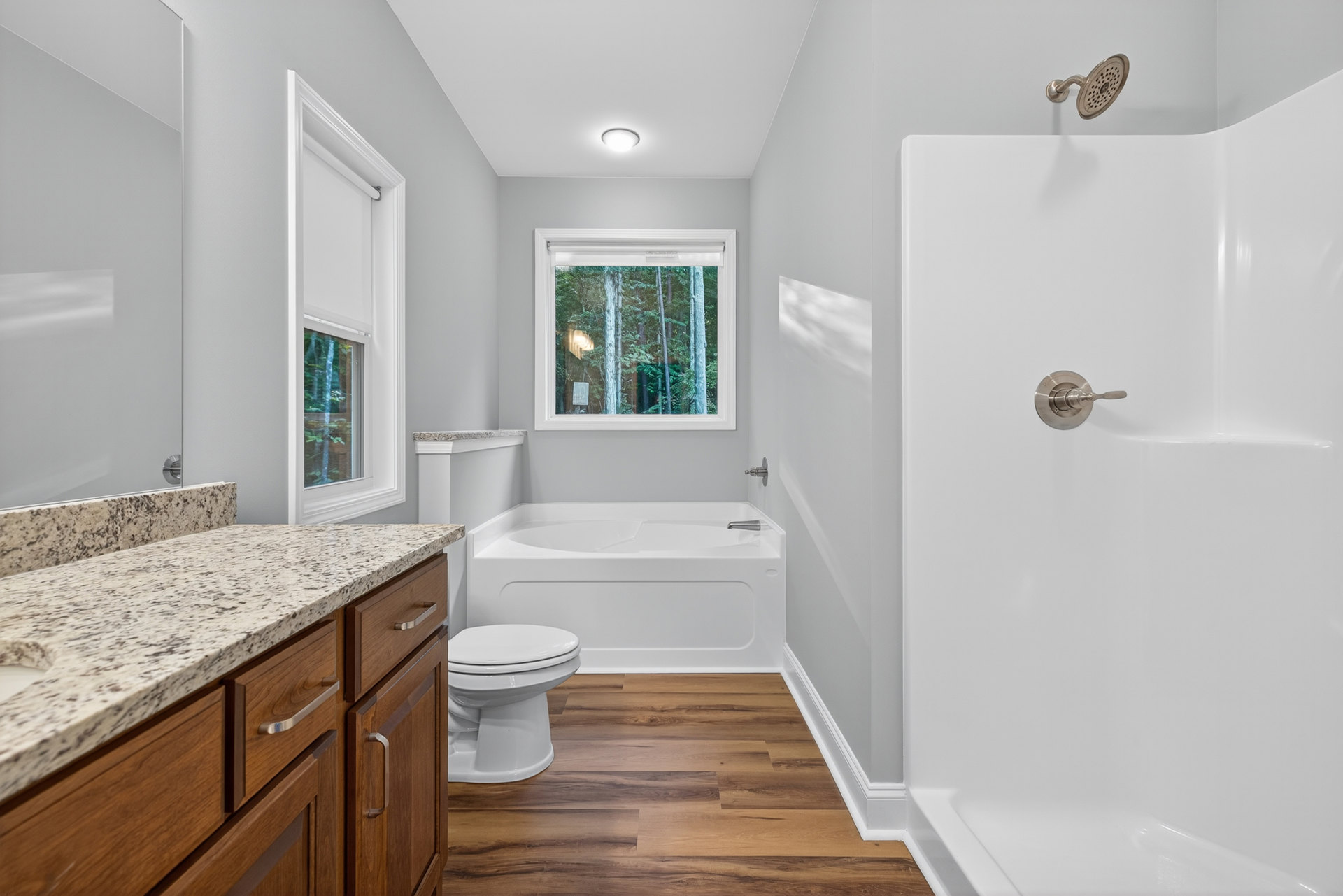 Bathroom featuring a freestanding white bathtub, marble countertop vanity with metal knob, white toilet, tiled walls, and a window with white frame overlooking trees.
