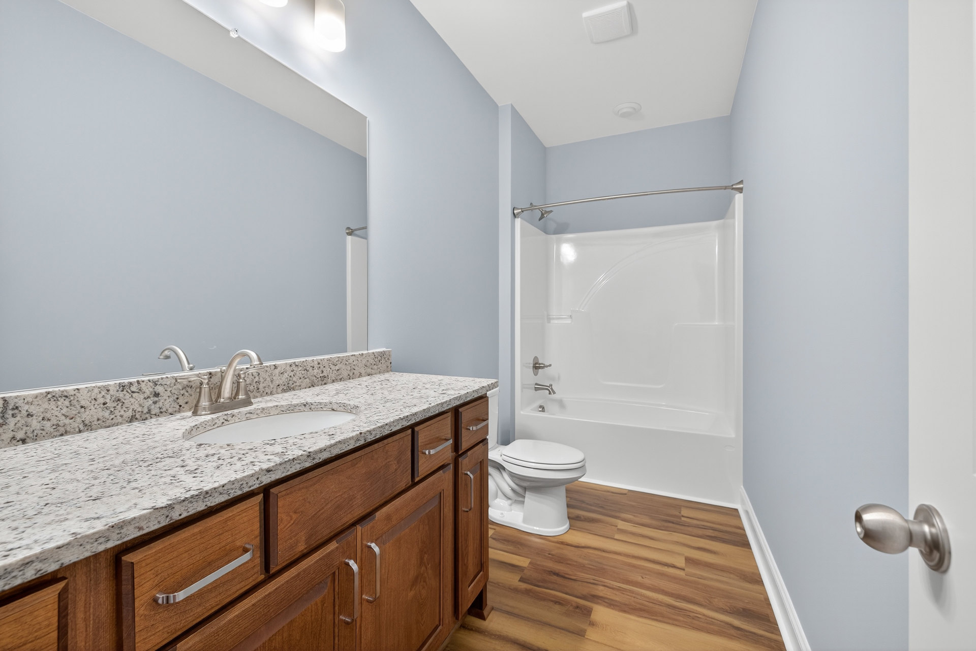 Bathroom with wood flooring, white toilet, glass-enclosed shower, white bathtub, white cabinetry with sink, chrome faucet, and close-up of brushed metal doorknob.
