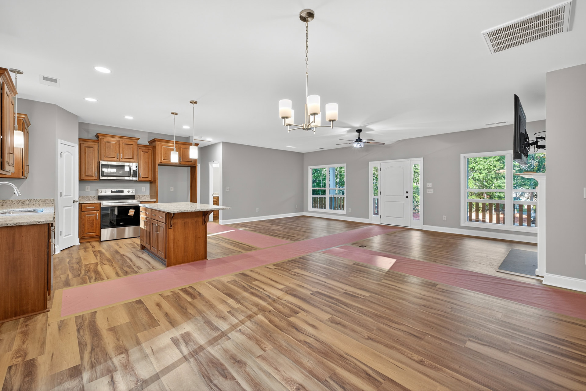 Spacious room with light hardwood floors, white kitchen island topped with marble, stainless steel stove and microwave, white door, modern cabinetry
