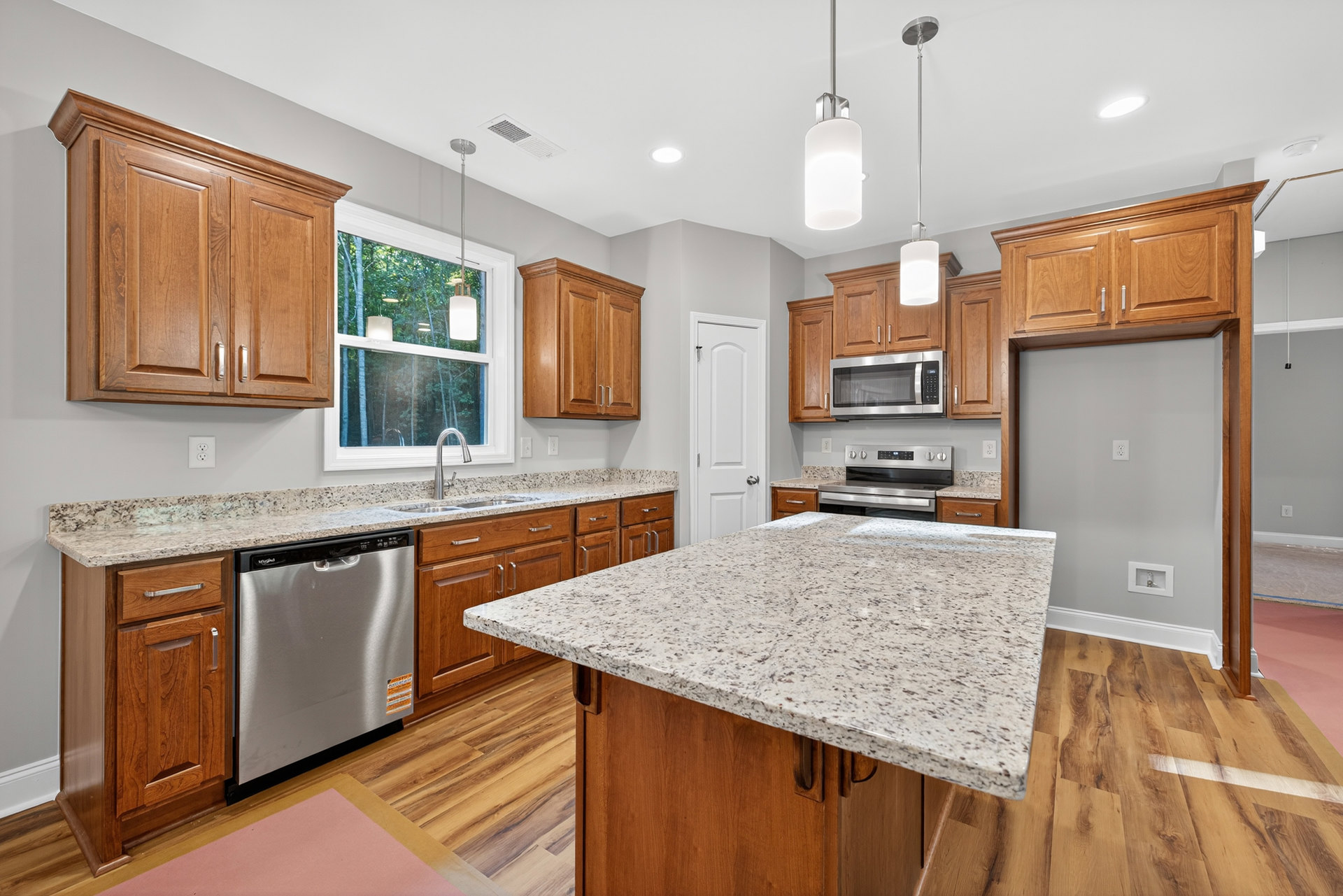 Granite kitchen island and countertops, stainless steel stove, microwave, and dishwasher, white cabinetry, window with pendant light fixture