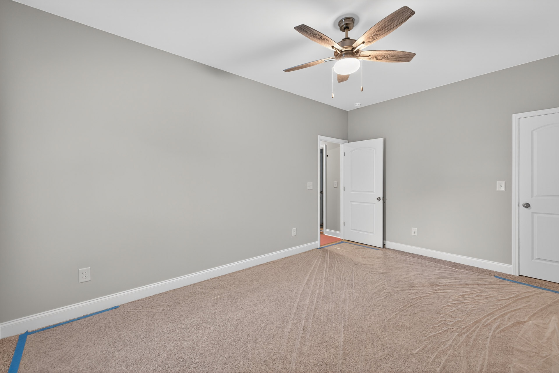 Ceiling fan with light fixture mounted on white plaster ceiling above laminate flooring, white door with silver handle, carpet repair tools visible on floor.