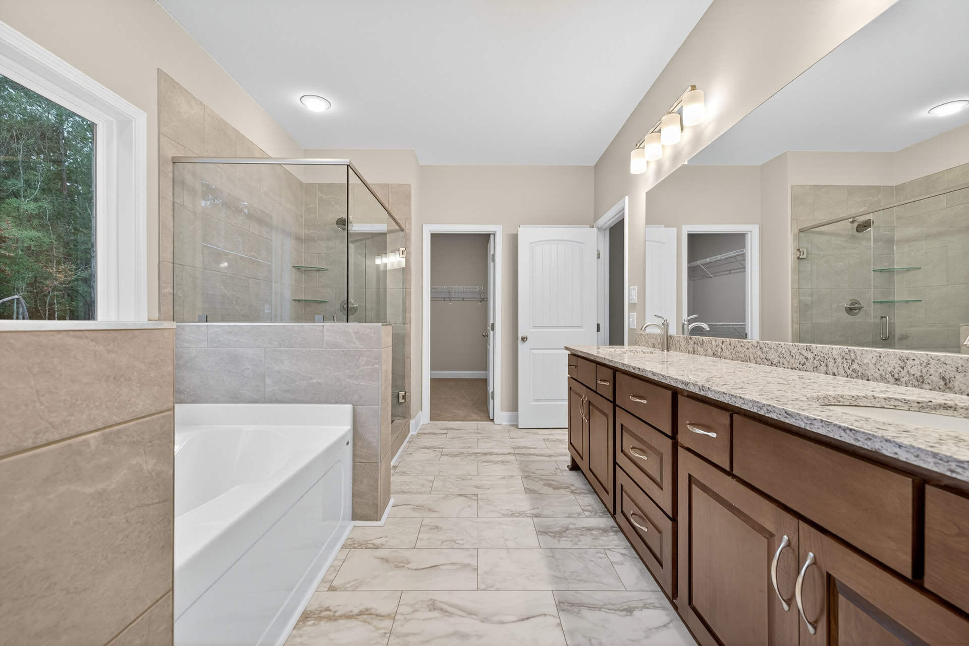 Bathroom with white bathtub, marble countertop sink, tile flooring, white closet door with shelf, and window overlooking trees