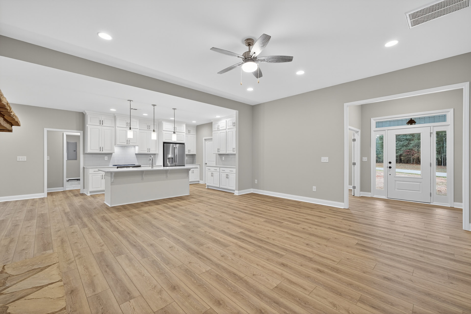 Spacious open kitchen with hardwood flooring, central island, stainless steel refrigerator, ceiling fan with light, white door featuring glass panes, and ceiling vent.