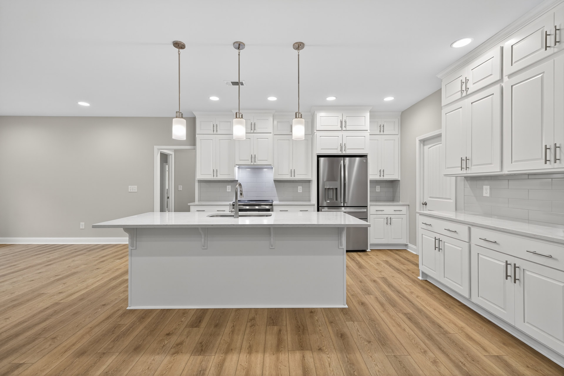 White kitchen with shaker cabinets, stainless steel refrigerator, wood plank flooring, quartz countertops, undermount sink, and recessed lighting.