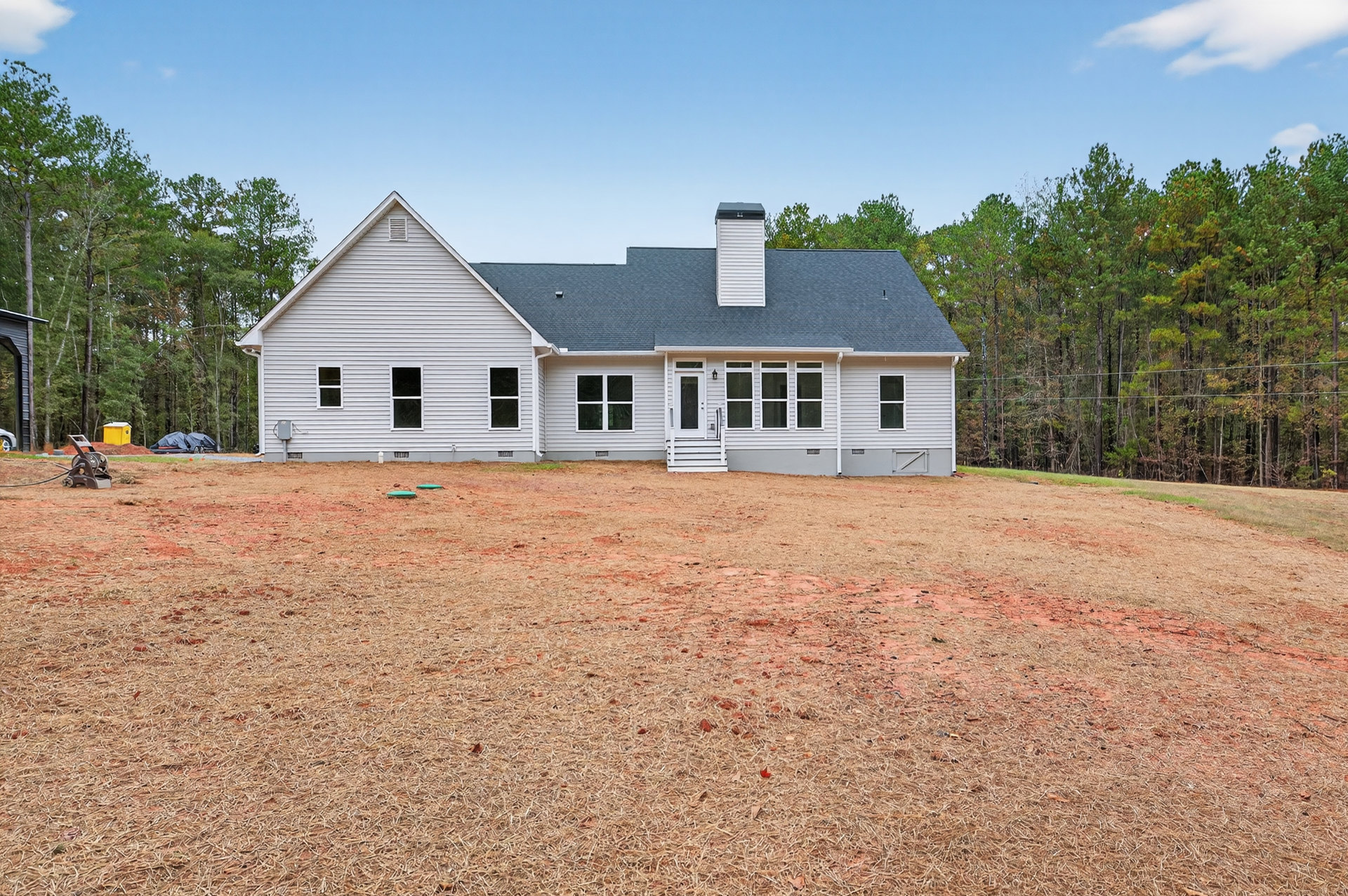 White siding house with chimney and white roof, set on a brown dirt yard under a blue sky with scattered clouds.