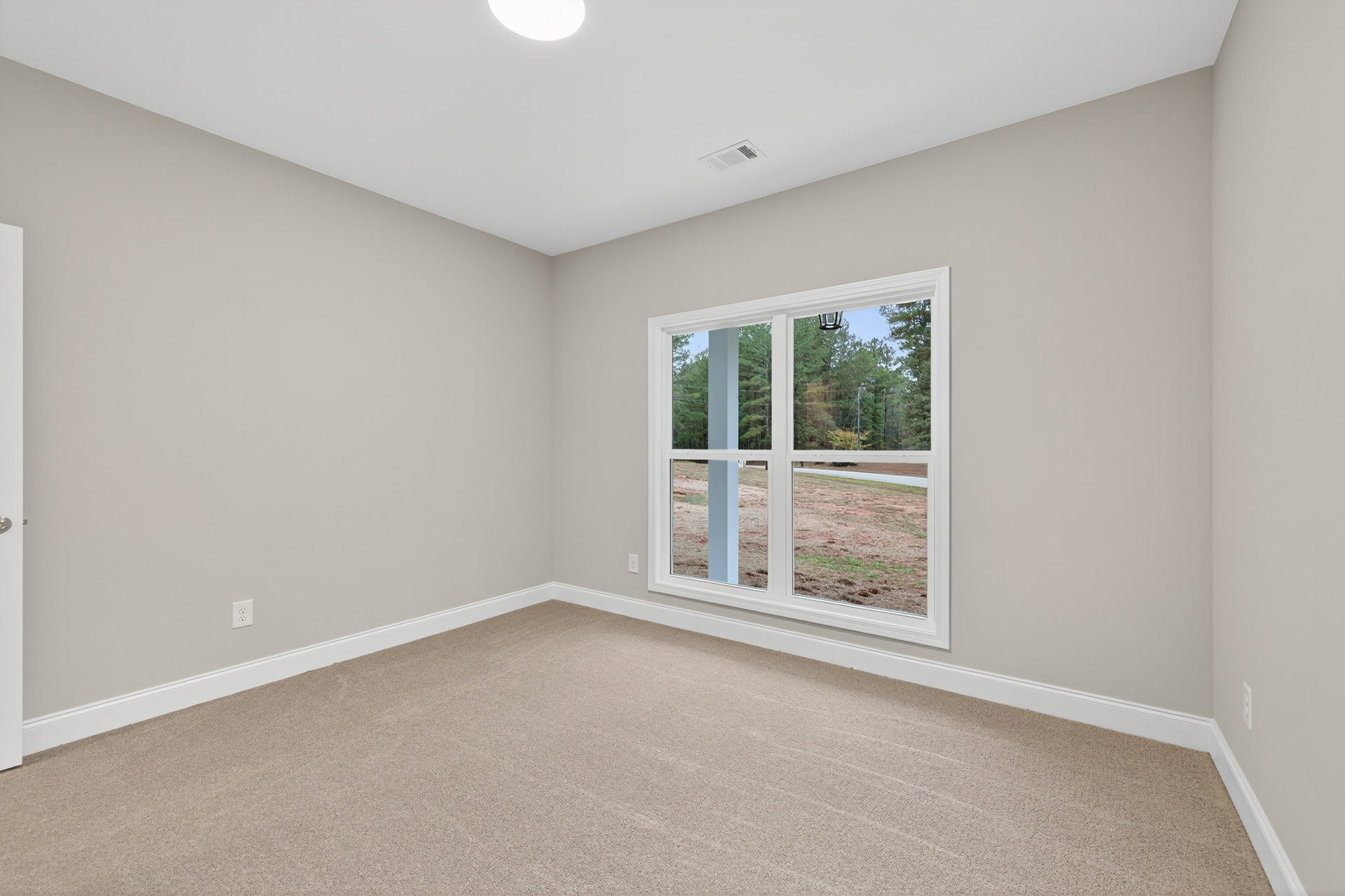Neutral-toned carpeted floor in a bright room with white plaster walls, large window framed by molding, and outdoor view of grassy field.