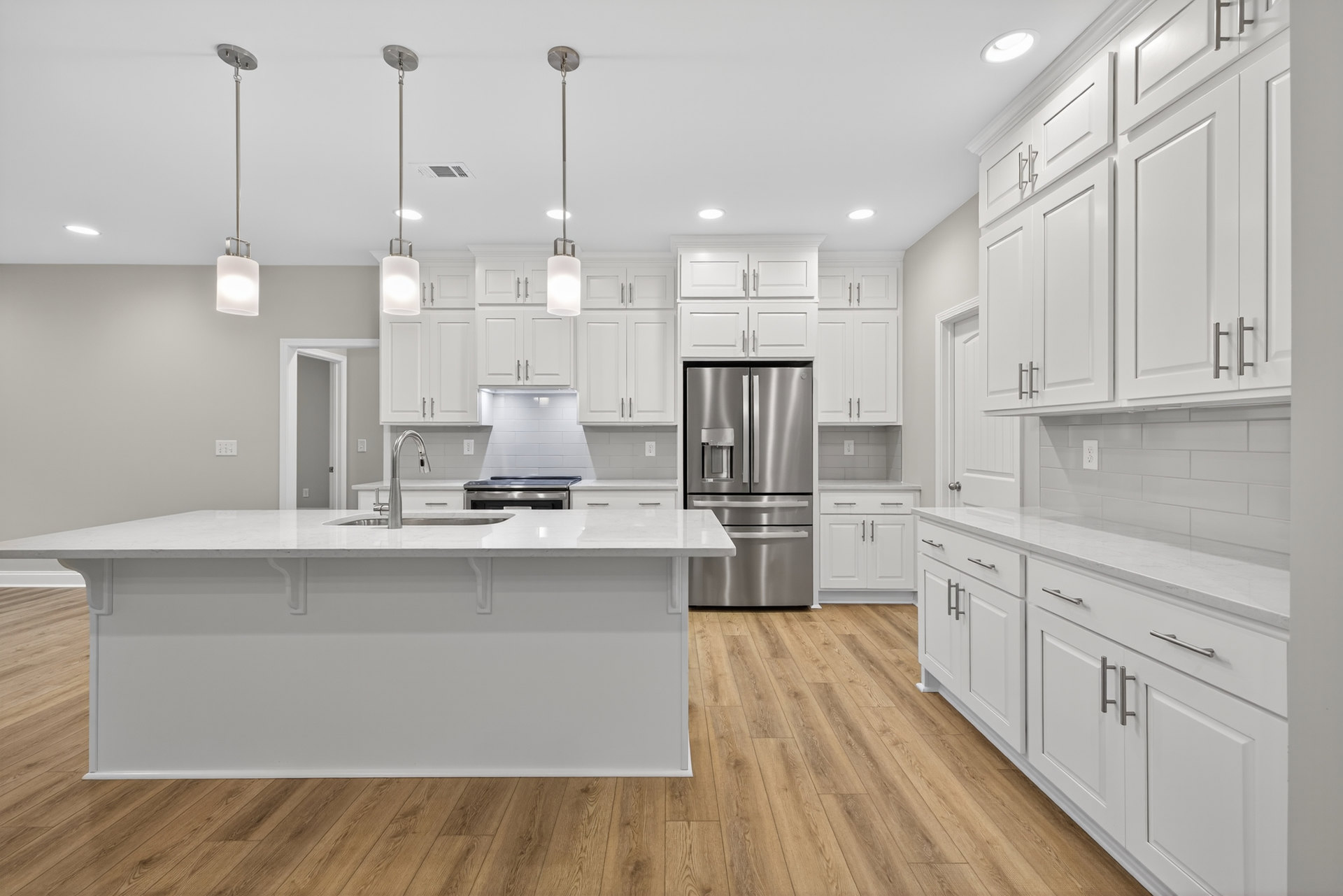 White shaker cabinets, stainless steel refrigerator with water dispenser, light gray tile backsplash, quartz countertops, undermount sink with chrome faucet, hardwood flooring