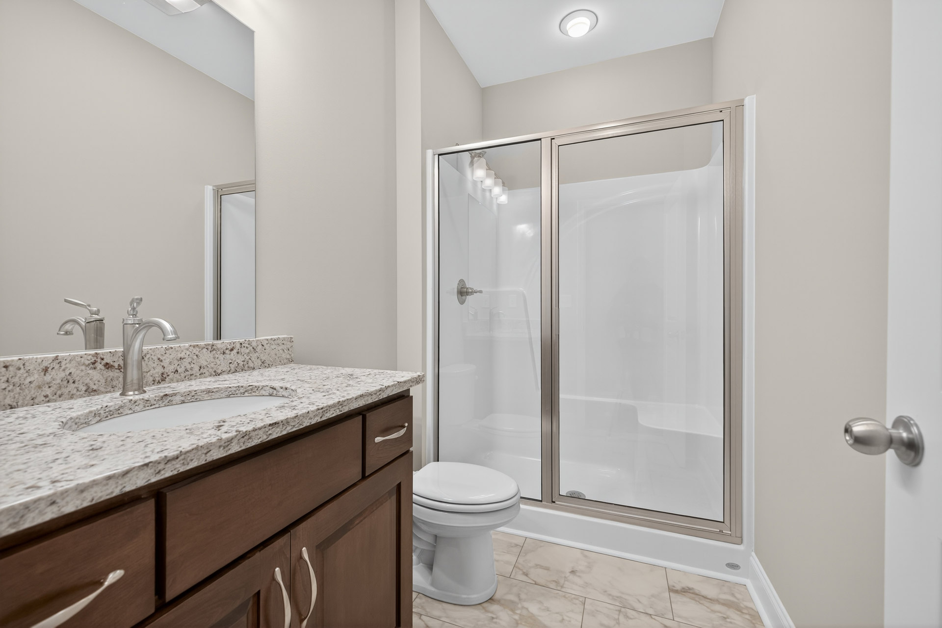 Modern bathroom featuring a glass-enclosed shower, white toilet with closed lid, wall-mounted sink with chrome faucet, tiled walls, and recessed lighting.
