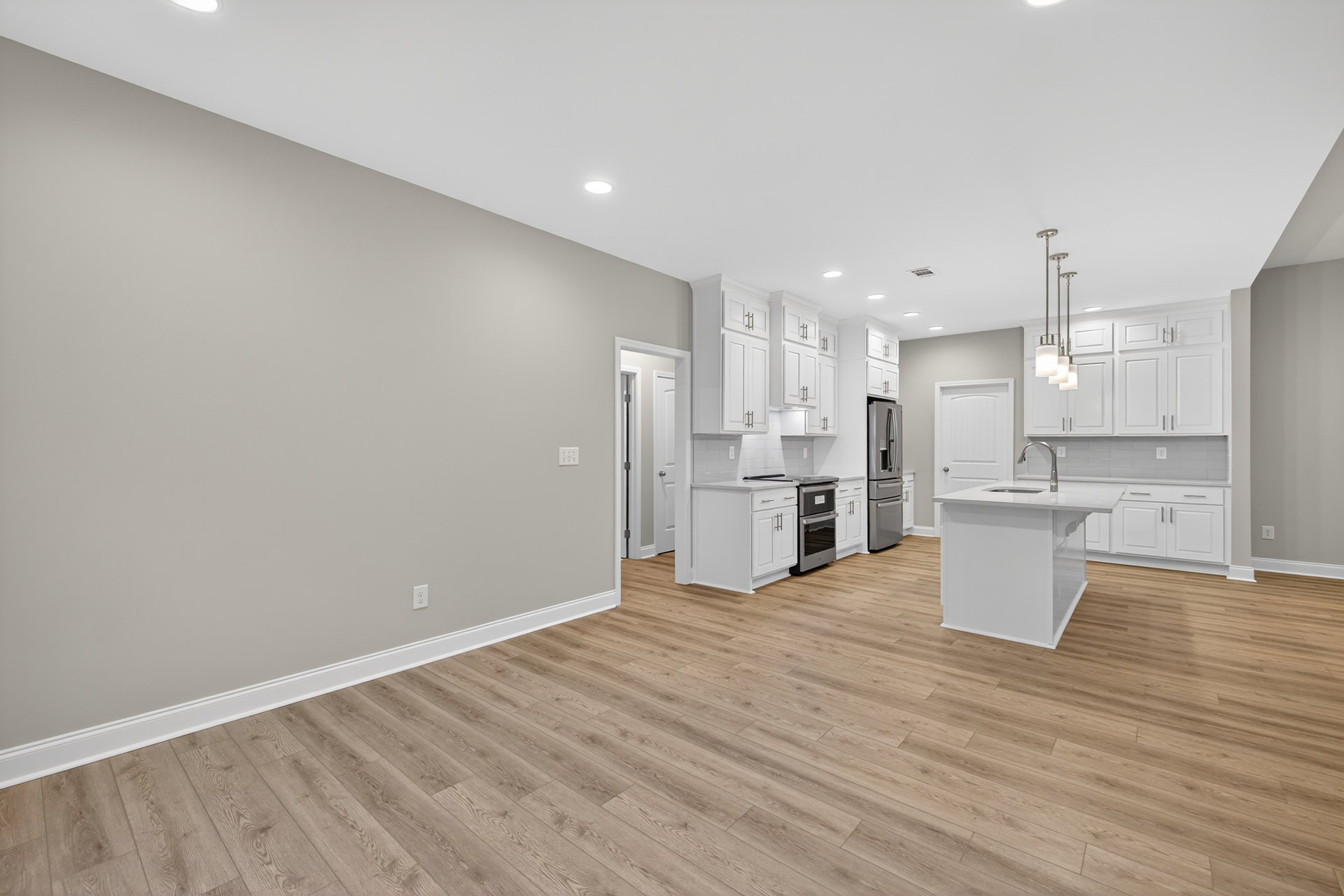 Open kitchen and dining area with hardwood flooring, white cabinetry, white kitchen island with built-in faucet, stainless steel stove, white door, and smooth white walls