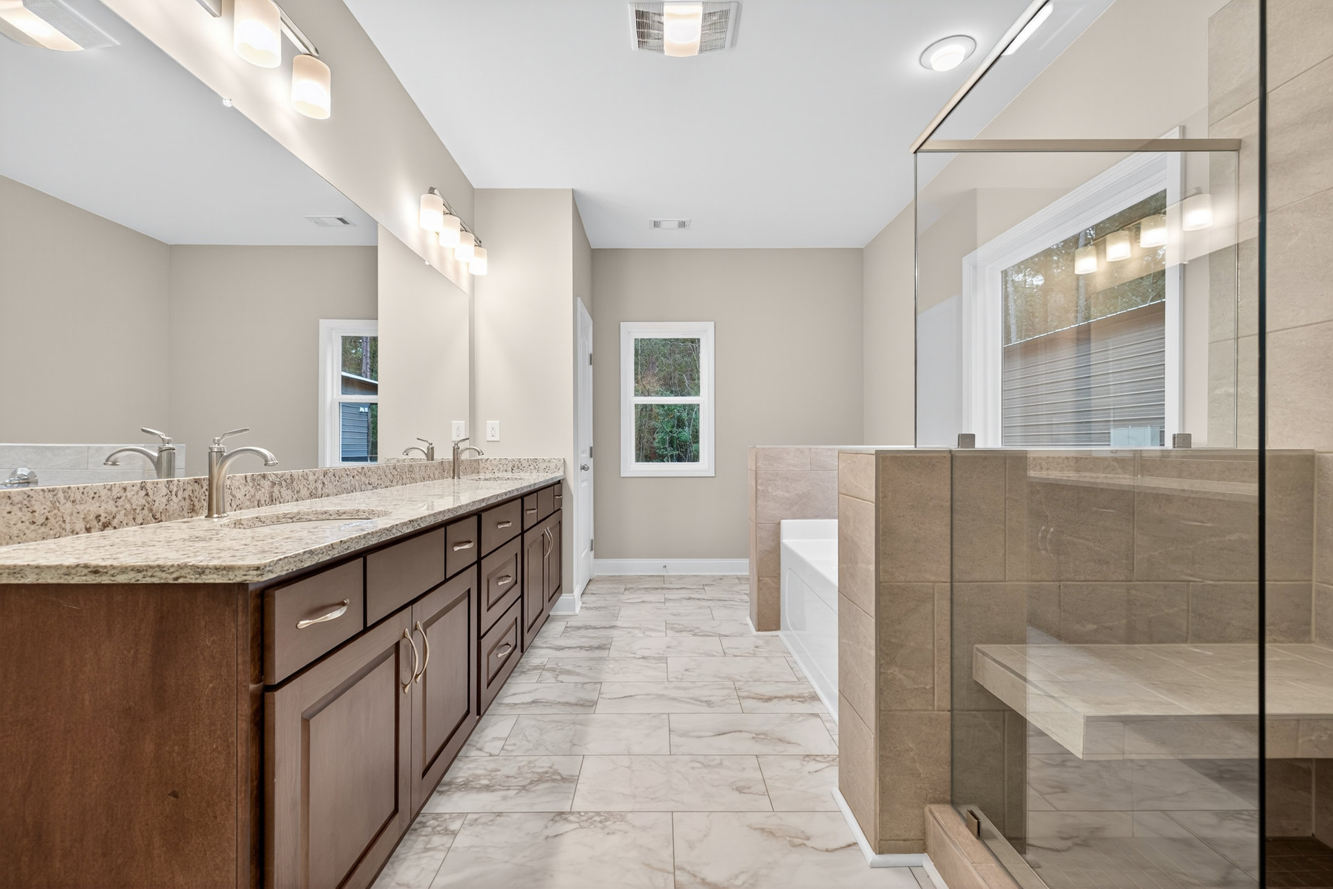 Bathroom with polished marble flooring, spacious glass-enclosed shower, marble countertops, modern sink, recessed lighting, and window overlooking leafy trees.