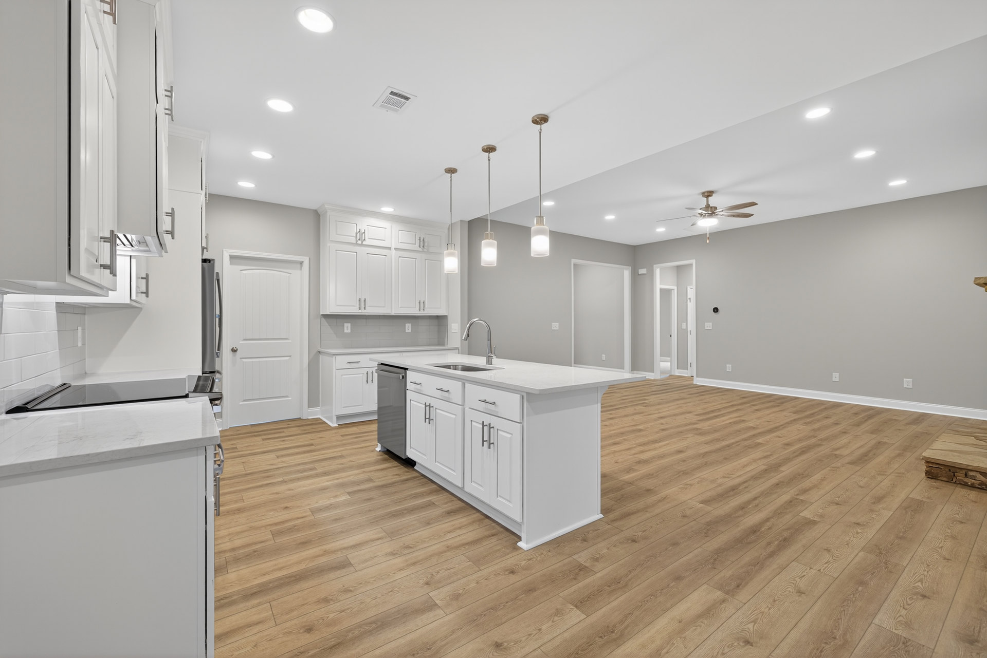 Kitchen with wood flooring, white island featuring a sink, white cabinetry, silver door handle, ceiling fan, recessed lighting, and light countertops.