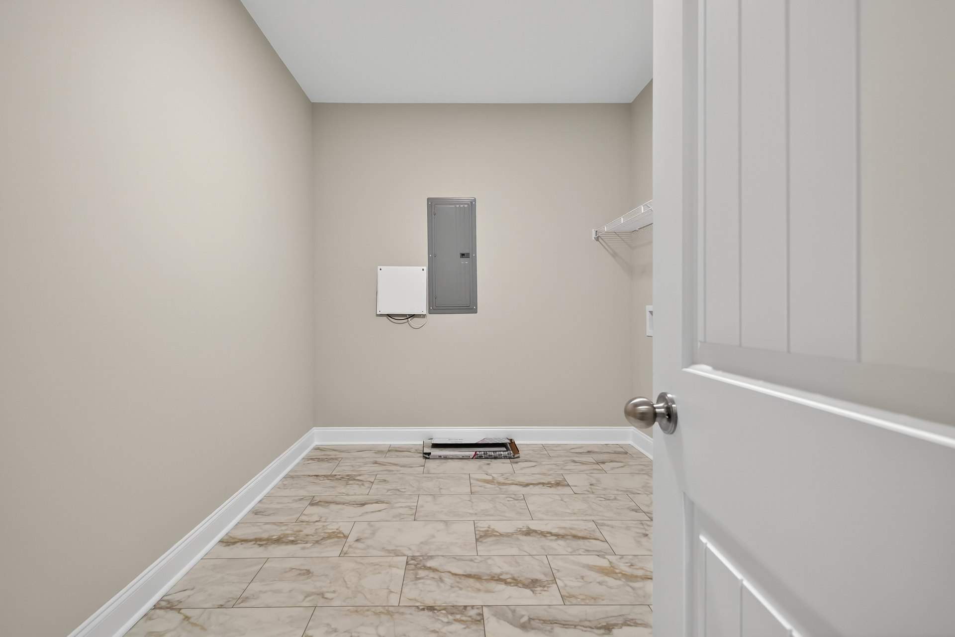 Tile flooring with white baseboards, grey door featuring a metal handle, white electrical outlet with black wires on plaster wall