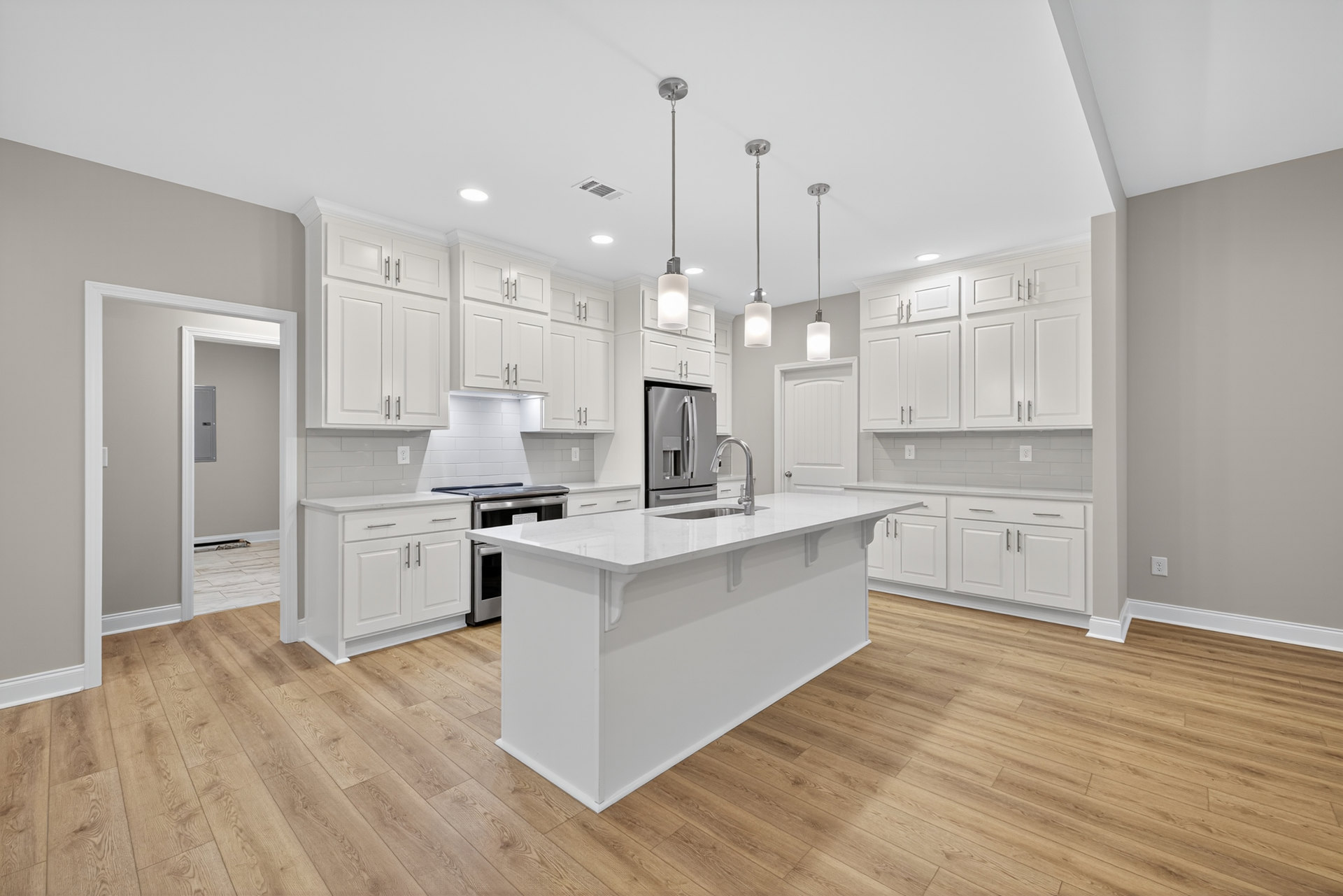 White kitchen with shaker cabinets, wood plank flooring, white island, stainless steel refrigerator, and quartz countertops