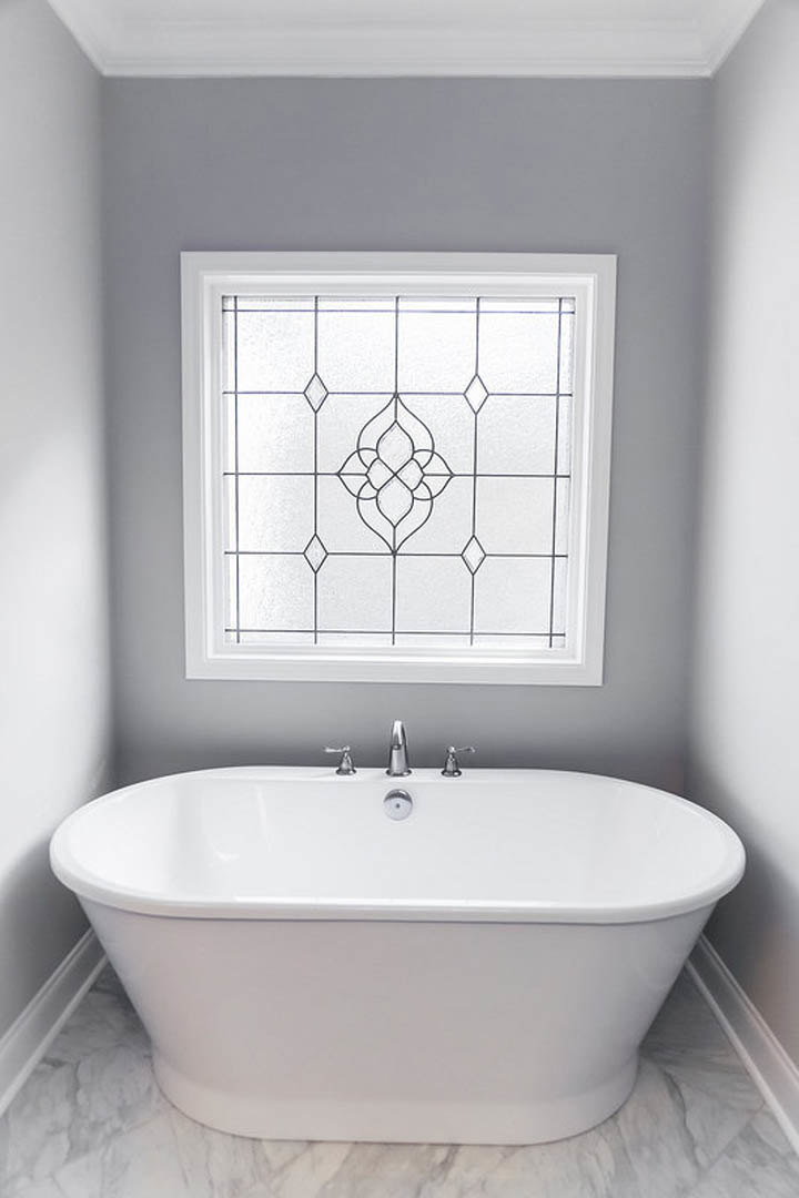 Freestanding white bathtub with chrome faucet on tiled floor, light gray walls, and modern bathroom fixtures