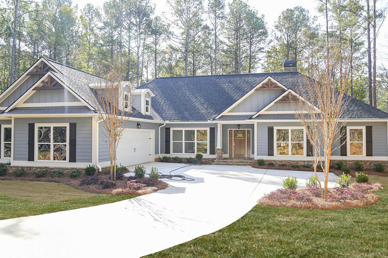 Two-story house with gray siding, white-trimmed windows, attached garage, concrete driveway, green lawn, and mature trees